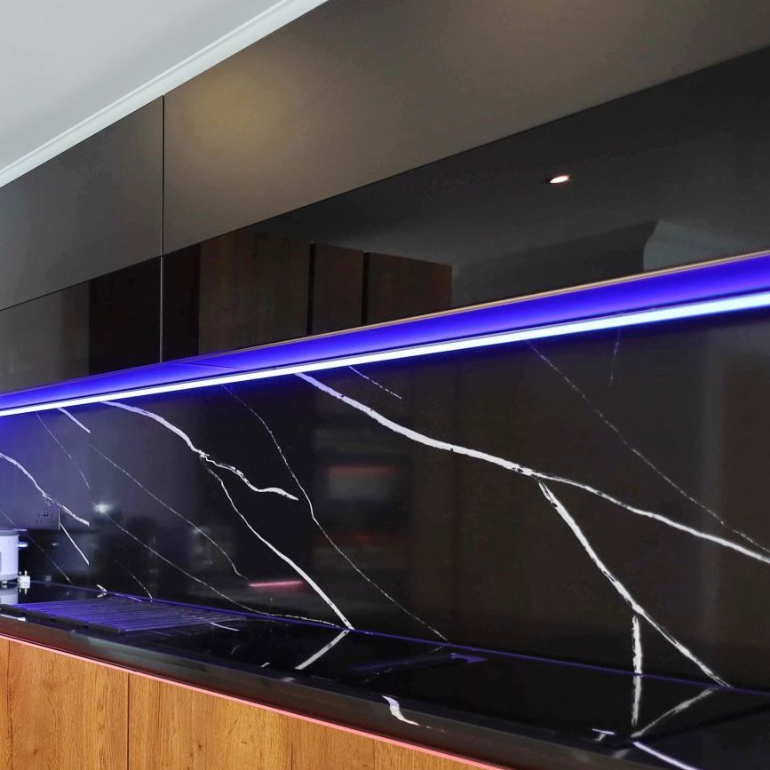 Black marble backsplash with white veining, under cabinet blue lighting, and wooden cabinetry.
