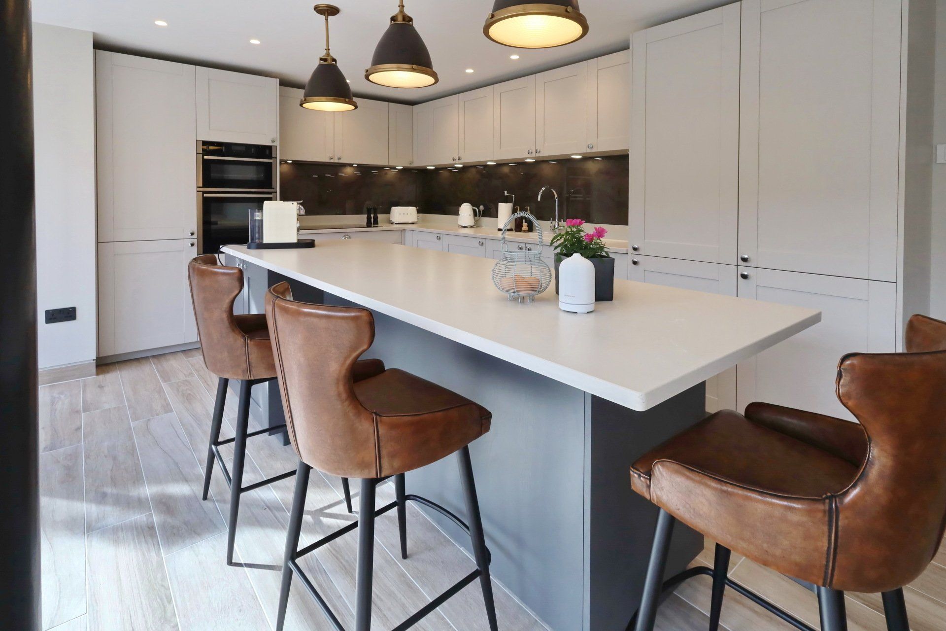 Modern kitchen with white cabinets, grey island, brown leather bar stools, and pendant lights.