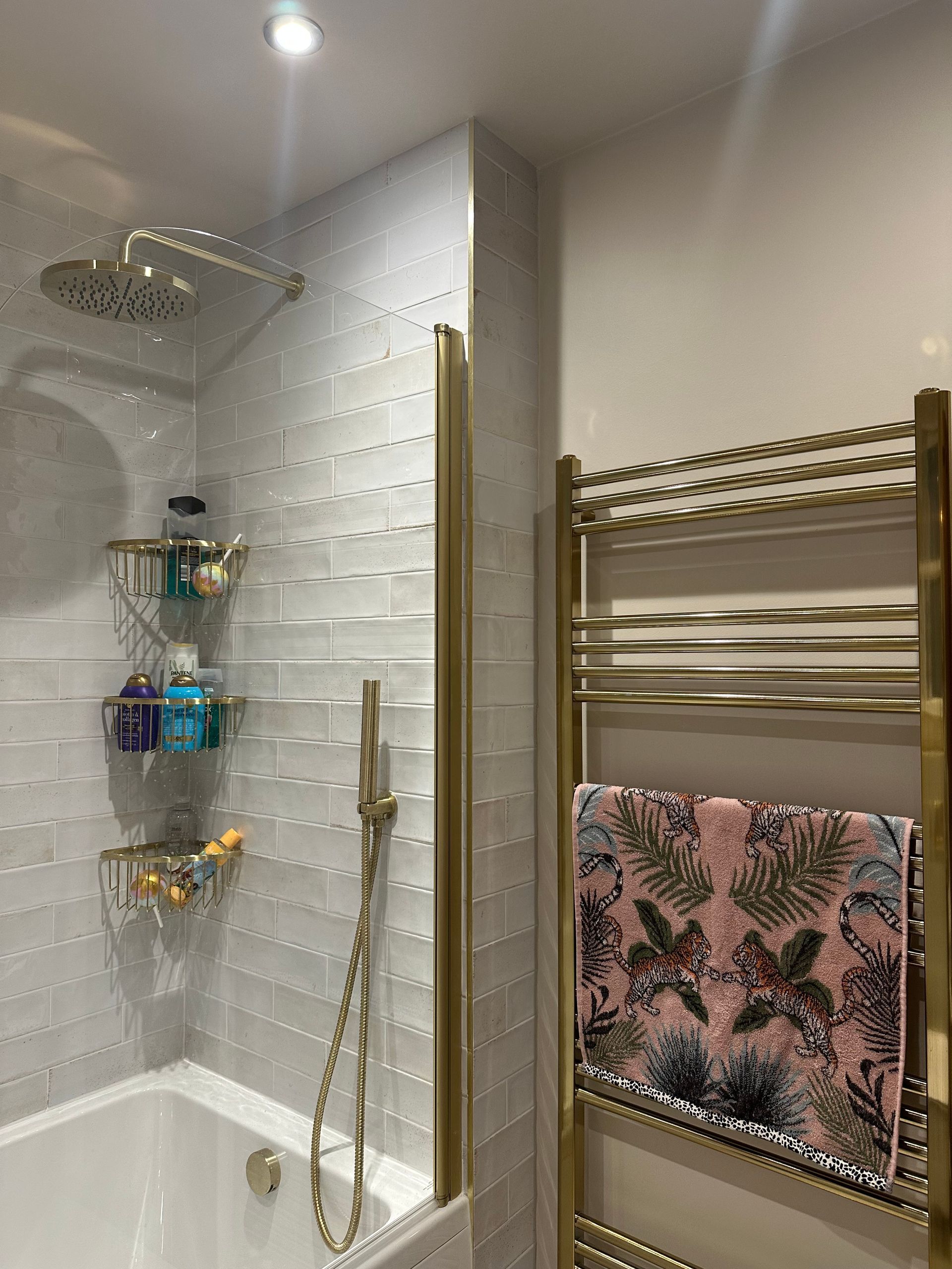 Bathroom with gold fixtures, textured gray tile, showerhead, towel rack with floral towel.