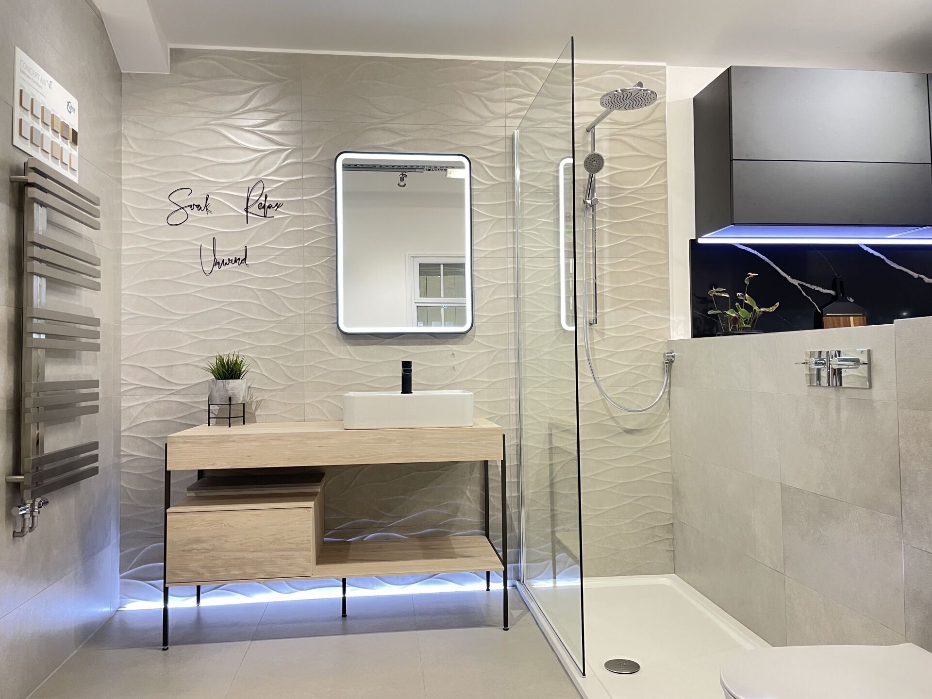 Modern bathroom with a light wood vanity, shower, and textured tile wall.