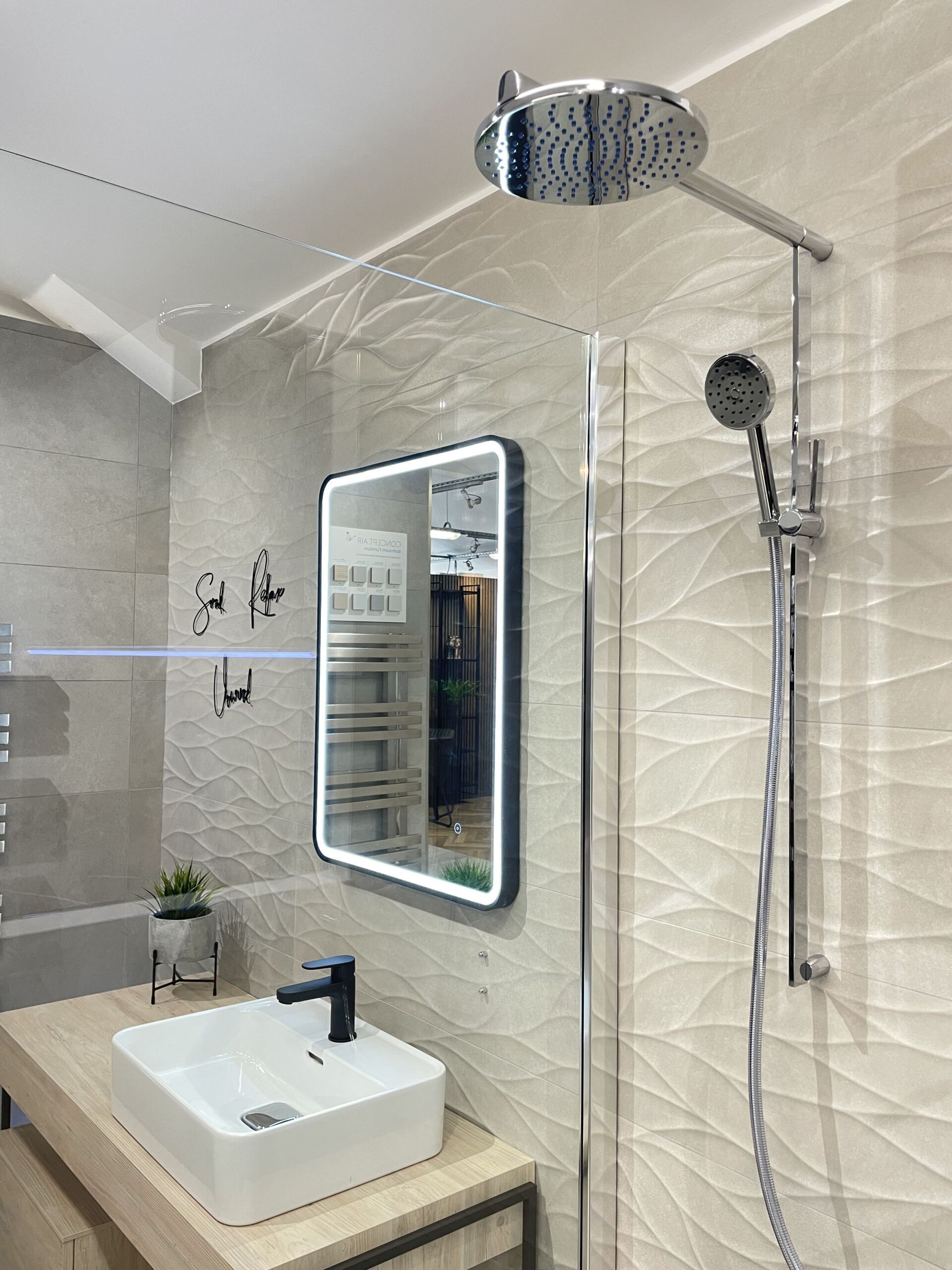 Modern bathroom with a showerhead, mirror, sink, and textured beige tile.