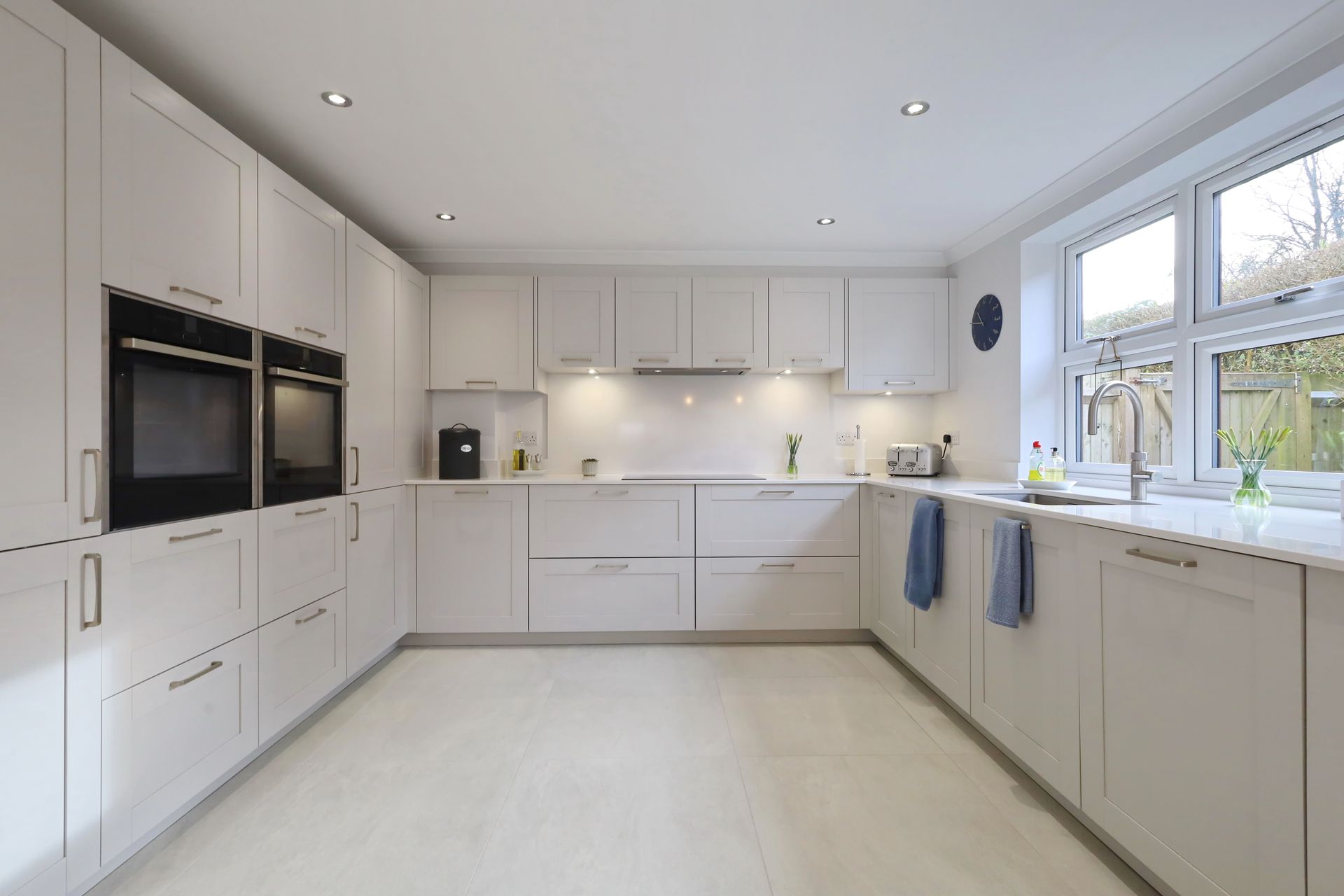 Modern white kitchen with built-in appliances, cabinets, and a window.