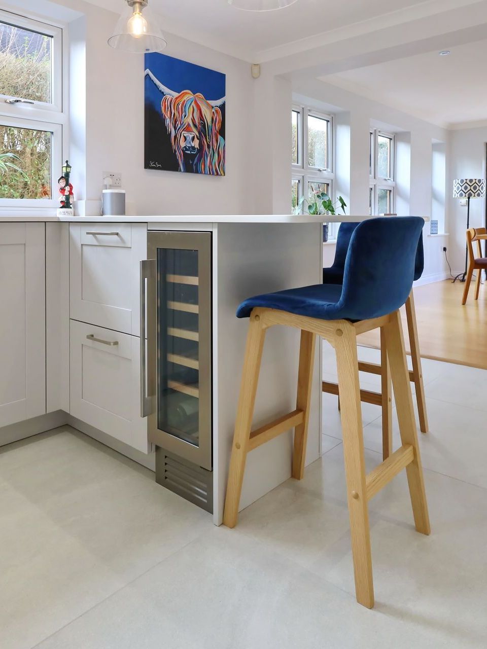 Kitchen island with built-in wine fridge, two blue velvet bar stools, and a painting of a Highland cow.