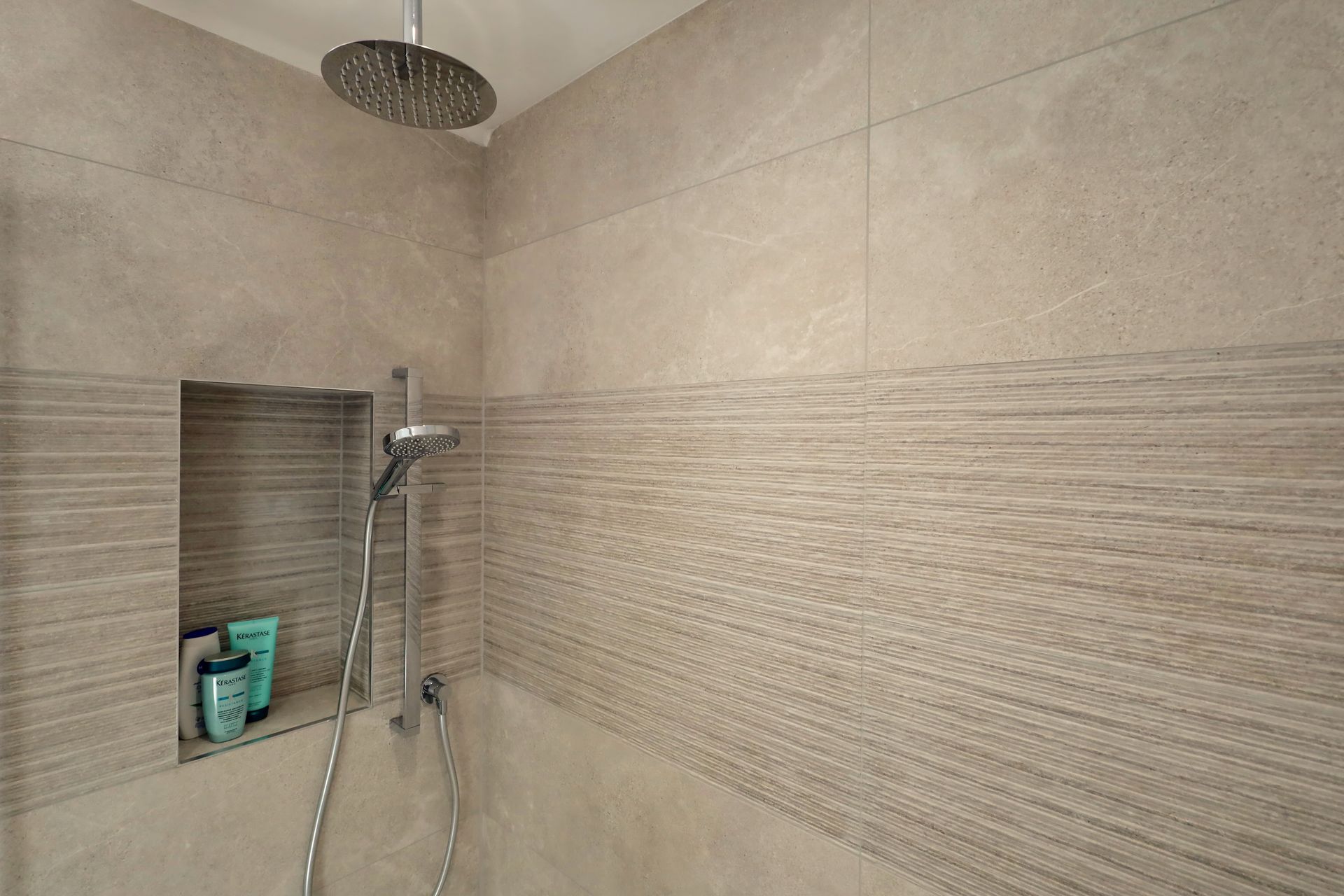 Shower with beige tile and a built-in shelf. A rain showerhead and handheld shower are visible.