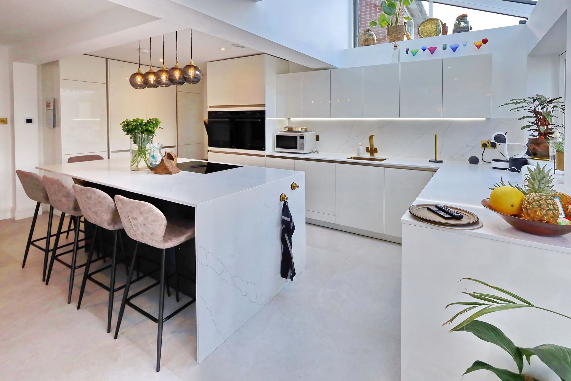 Modern white kitchen with a large island, stools, and pendant lighting.