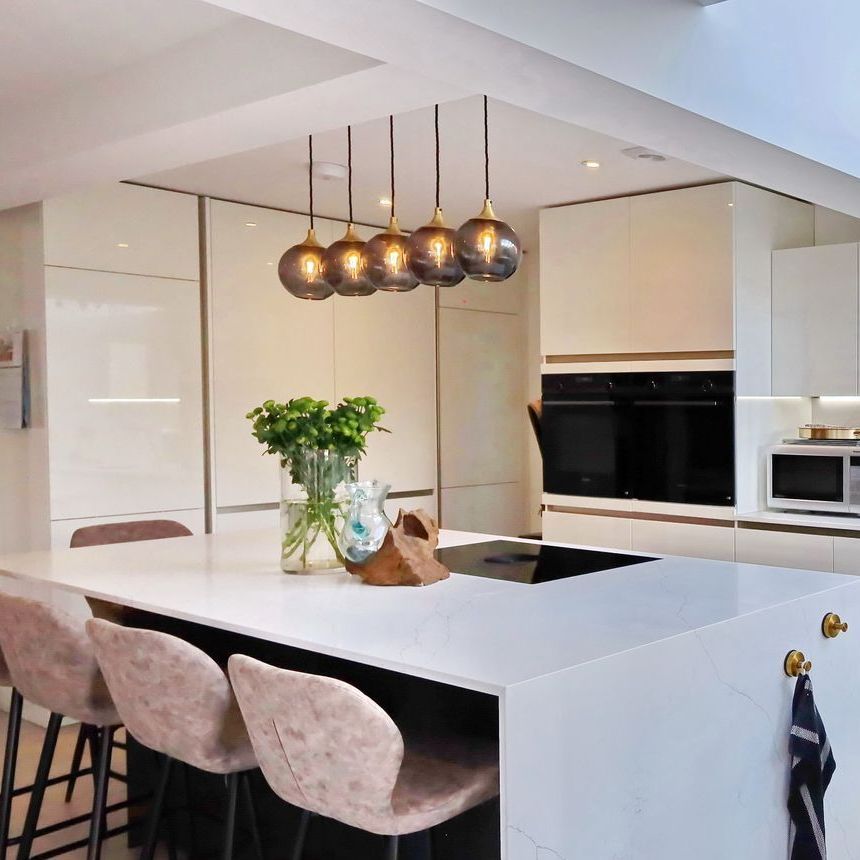 Modern kitchen with white countertops, island with seating, pendant lights, and built-in appliances.
