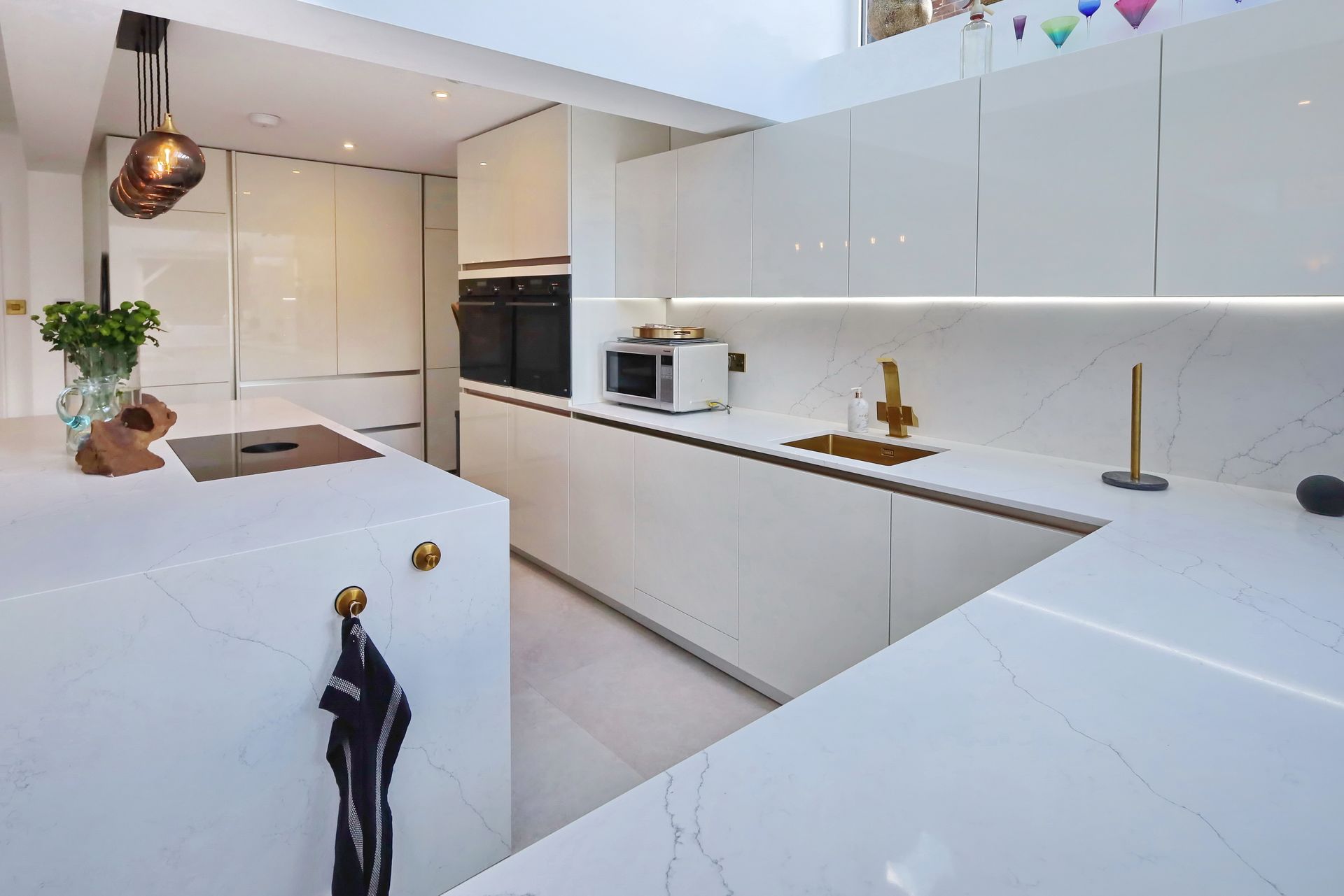Modern white kitchen with island, marble countertops, built-in appliances, and gold fixtures.