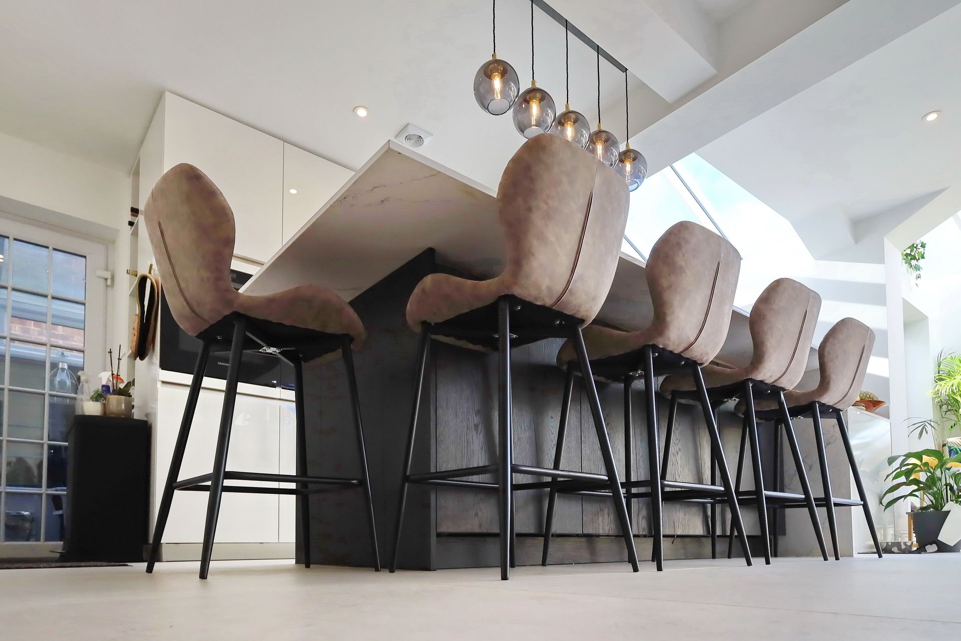 Kitchen island with six tall, upholstered bar stools. Modern design with pendant lights.