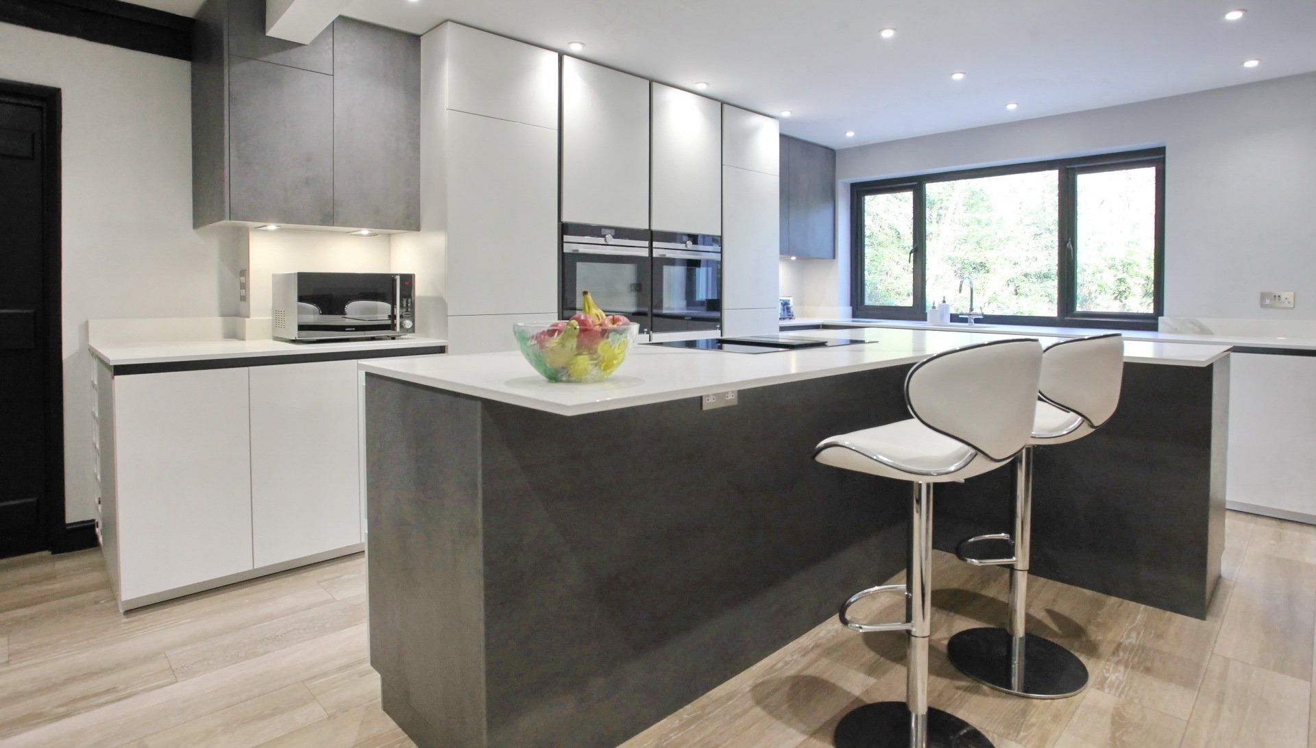 Modern kitchen with gray and white cabinets, island with stools, and large window.