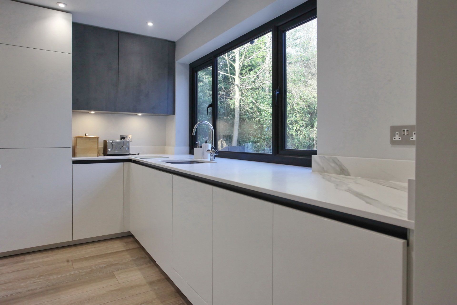 Modern white kitchen with a large window and gray cabinets.