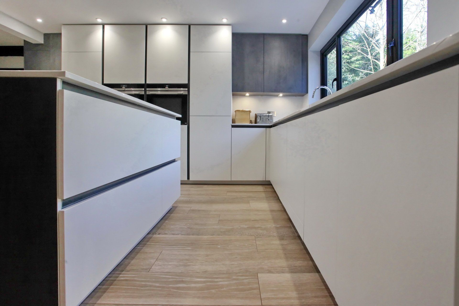Modern white kitchen with wood flooring and dark trim accents.