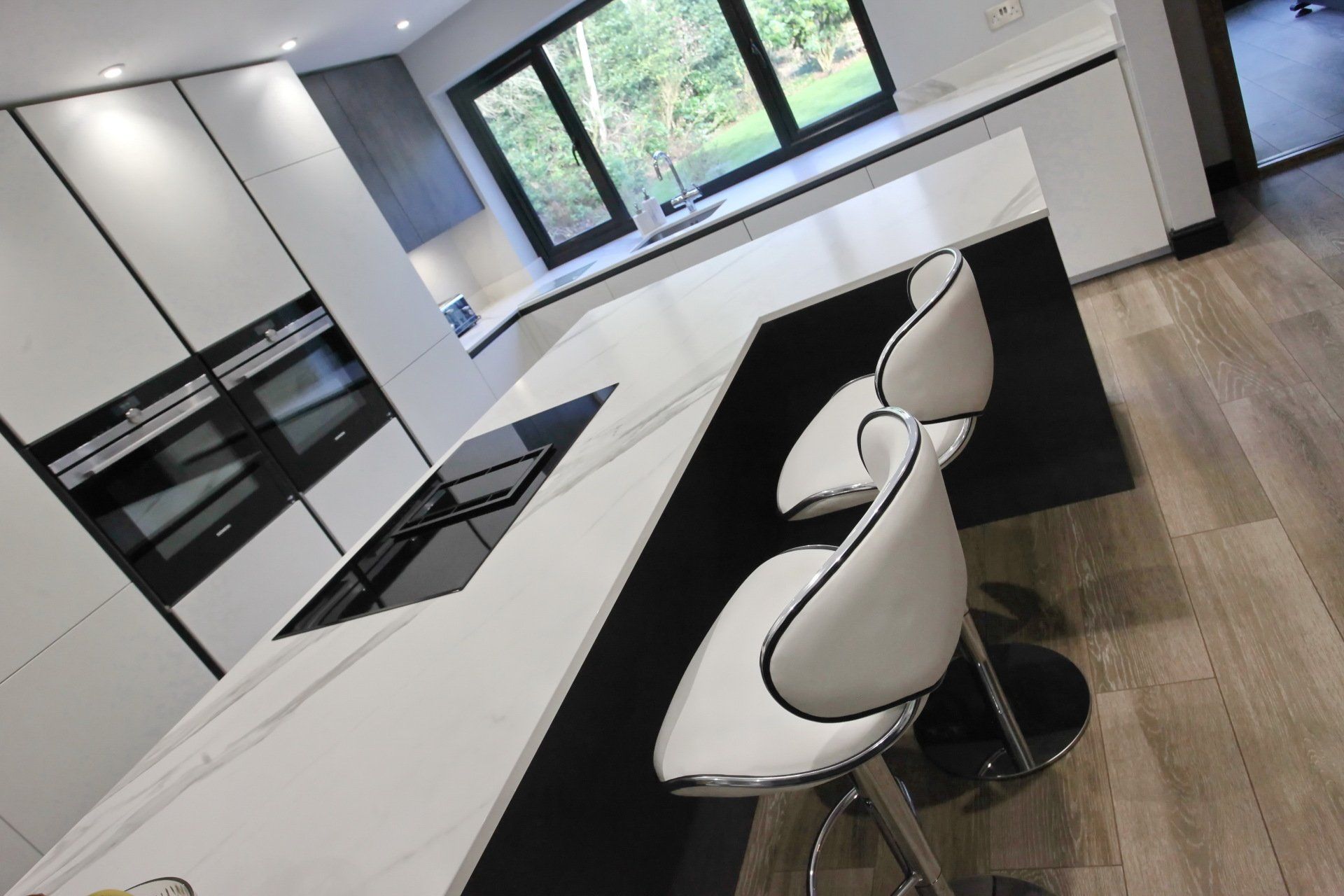 Modern kitchen with white countertops and black cabinets; white bar stools.