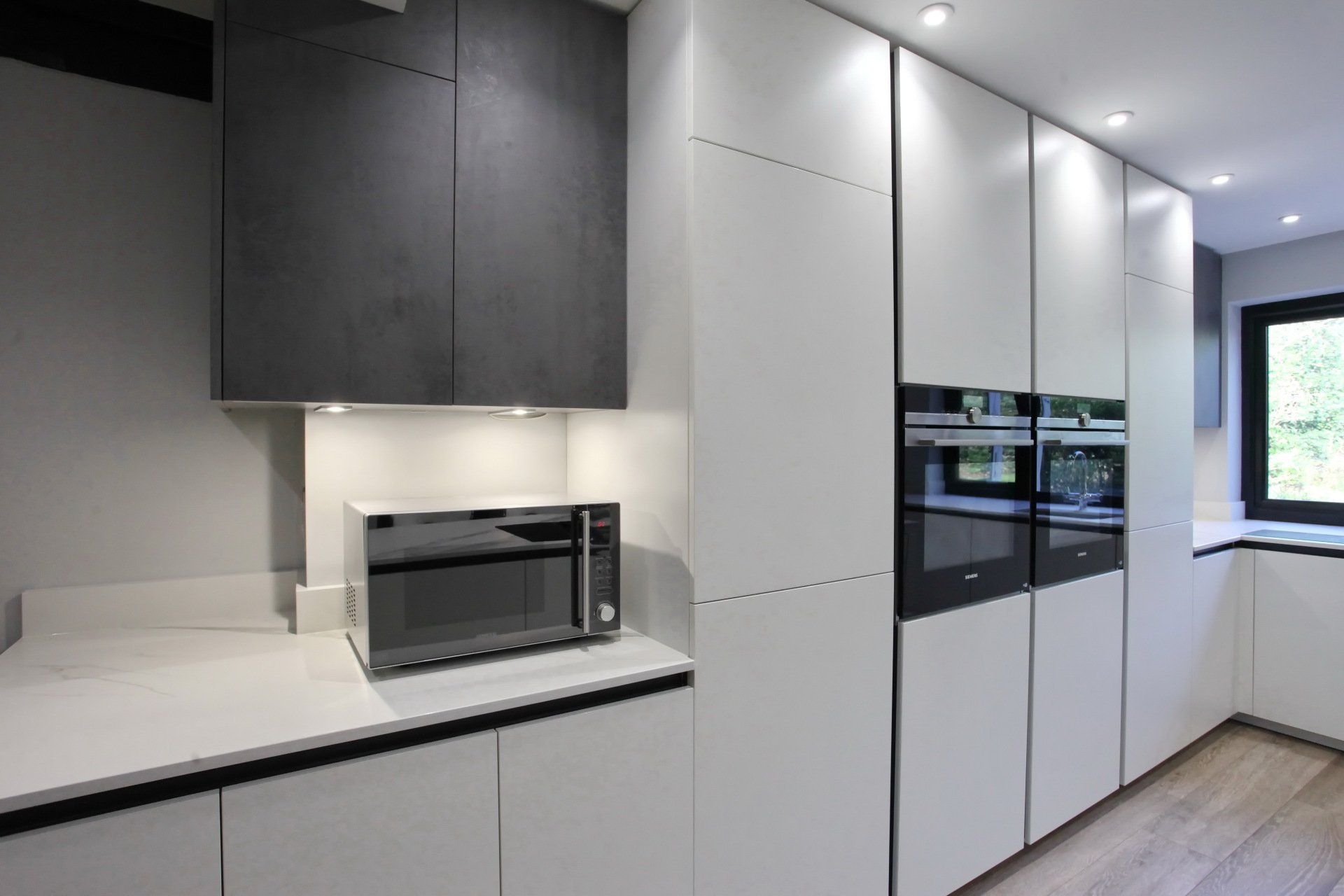 Modern kitchen with white cabinetry, built-in ovens, microwave, and dark gray upper cabinet.