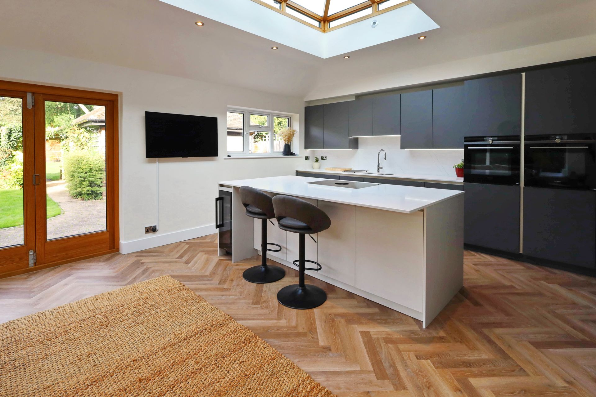 Modern kitchen with white island, gray cabinets, and herringbone wood floor.