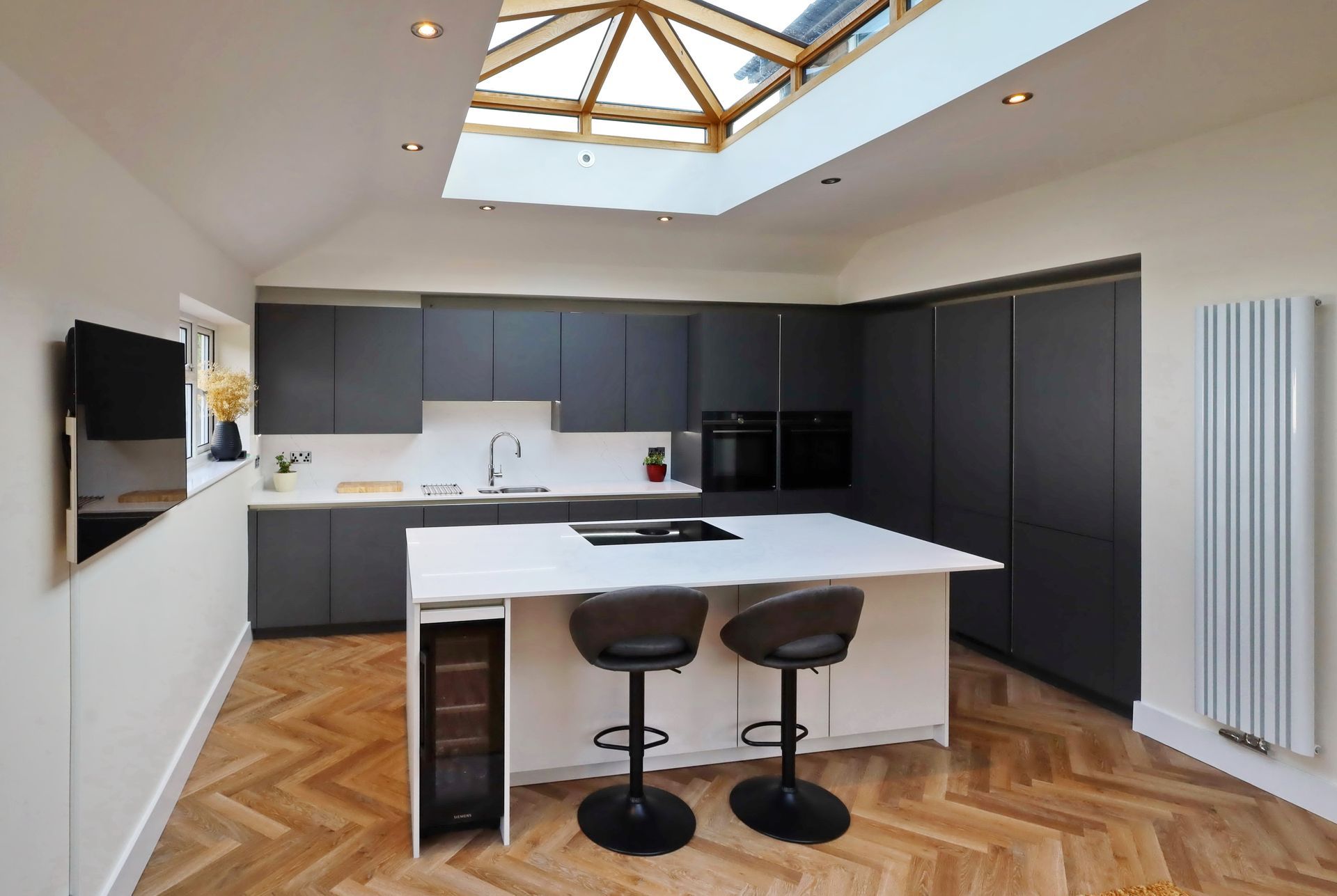 Modern kitchen with dark gray cabinets, white island, wood flooring, and skylight.