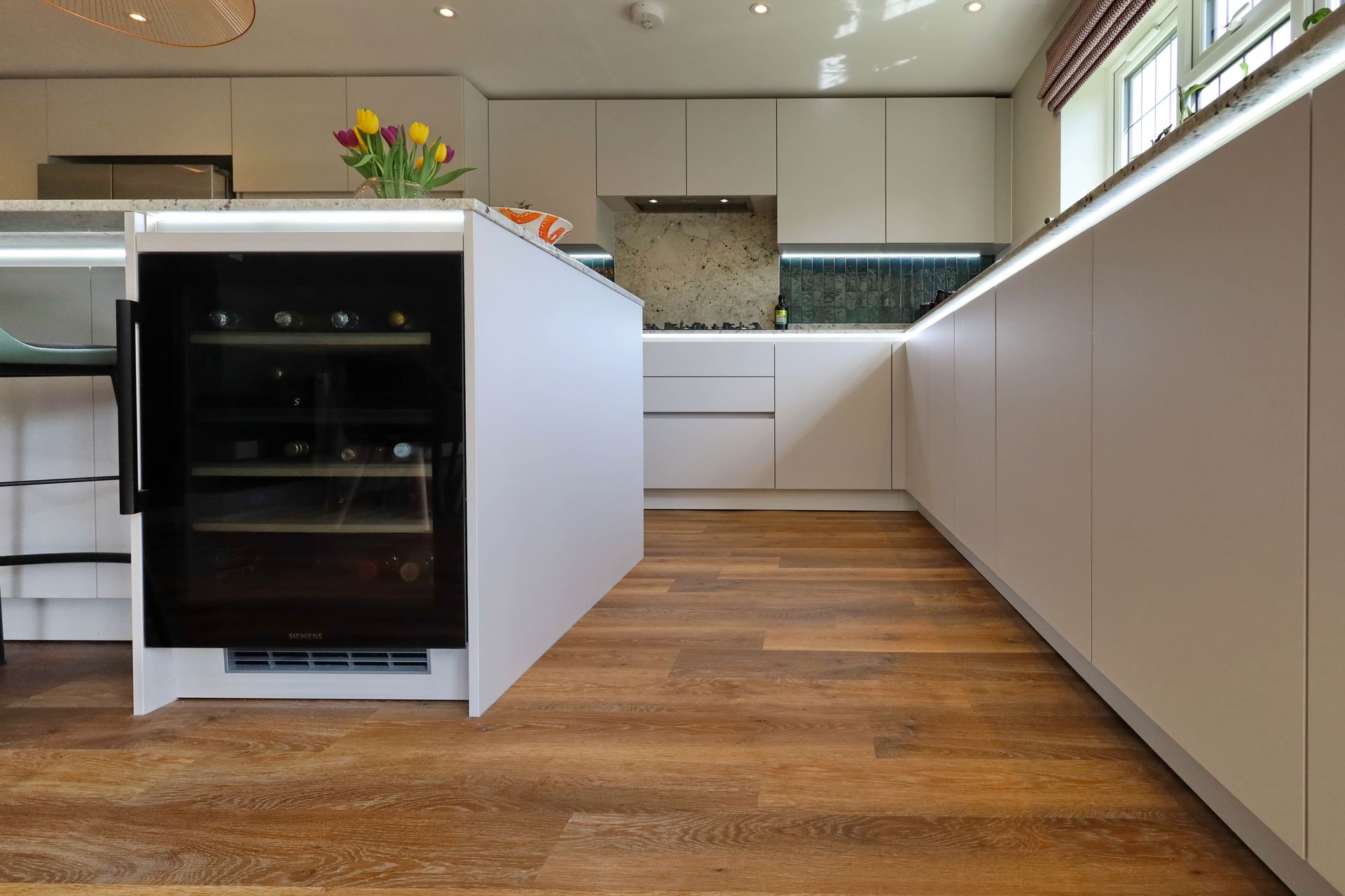 Modern white kitchen with wooden floors. Wine fridge integrated in island.