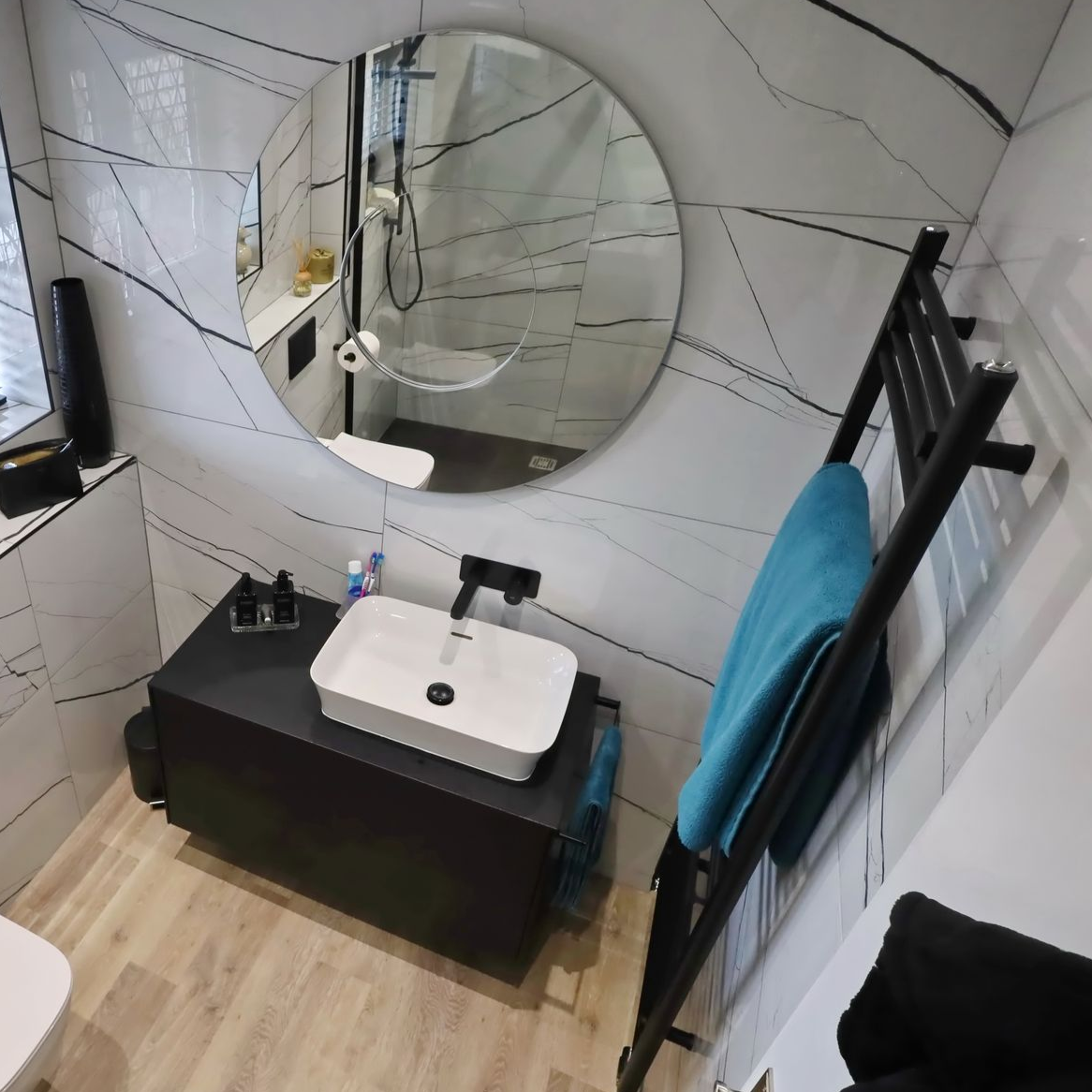 Modern bathroom with white and black marbled tile, round mirror, black vanity, and towel ladder.