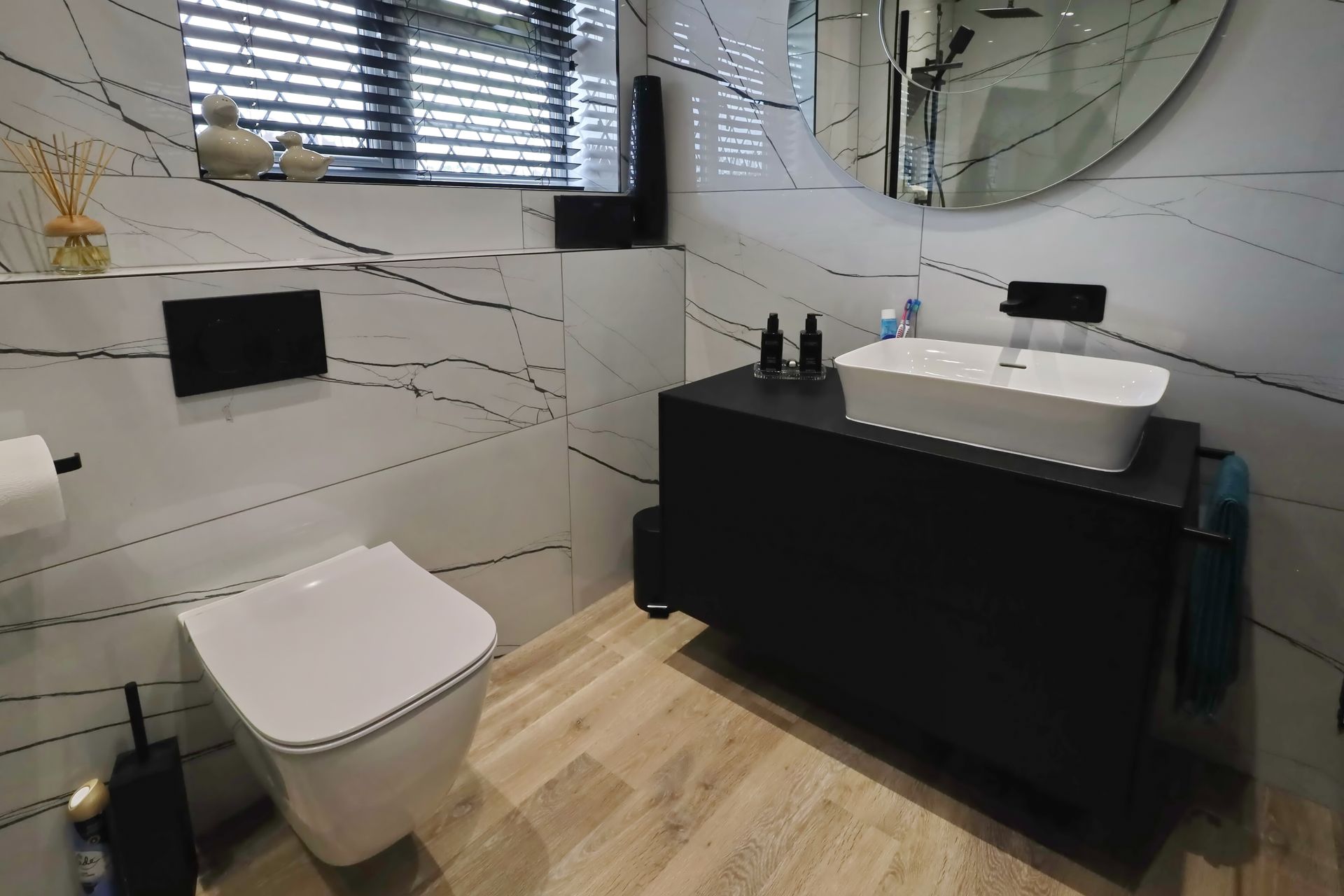 Modern bathroom with white and black marble-look tile, black vanity, and white toilet.