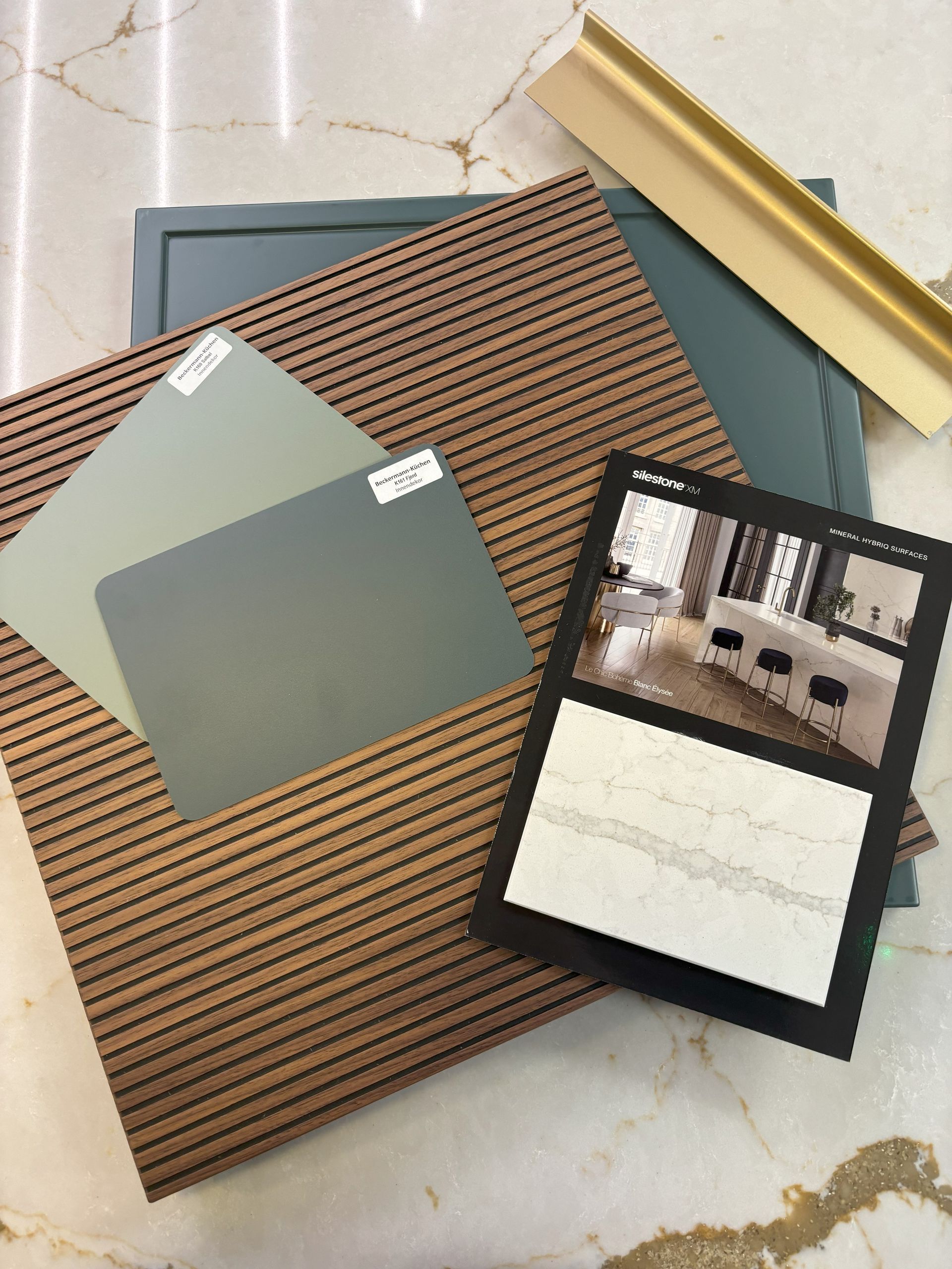 Samples of wood, paint, and a frame in teal, beige, and gray, with a photo of a kitchen.