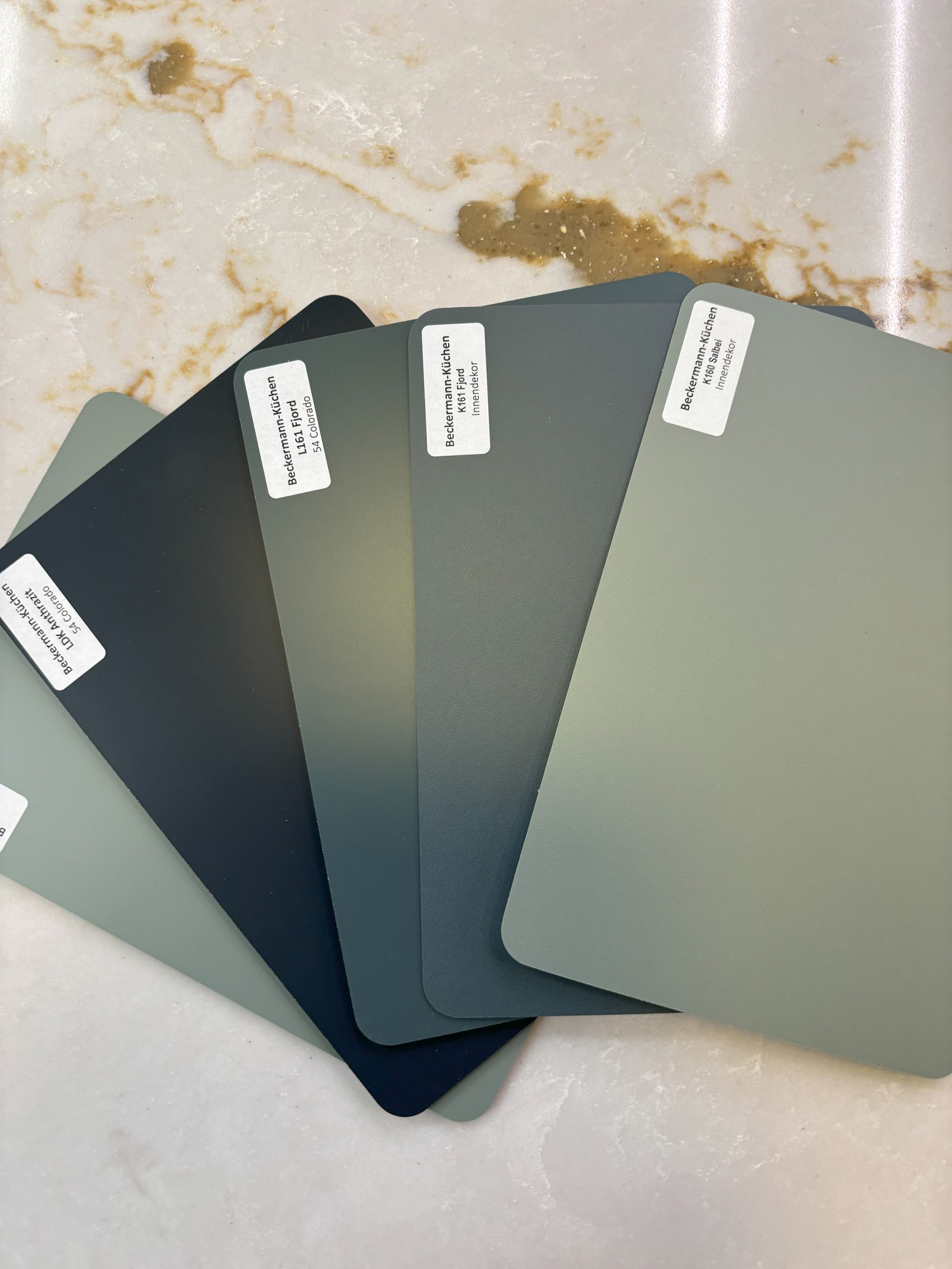 Samples of muted green-blue paint colors arranged on a marbled surface.