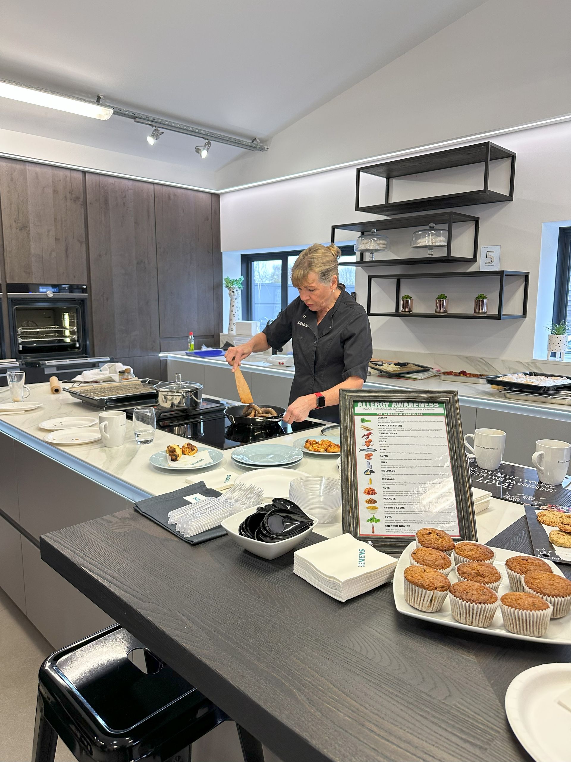 Chef stirring food in a pan on a kitchen island during a cooking demonstration.