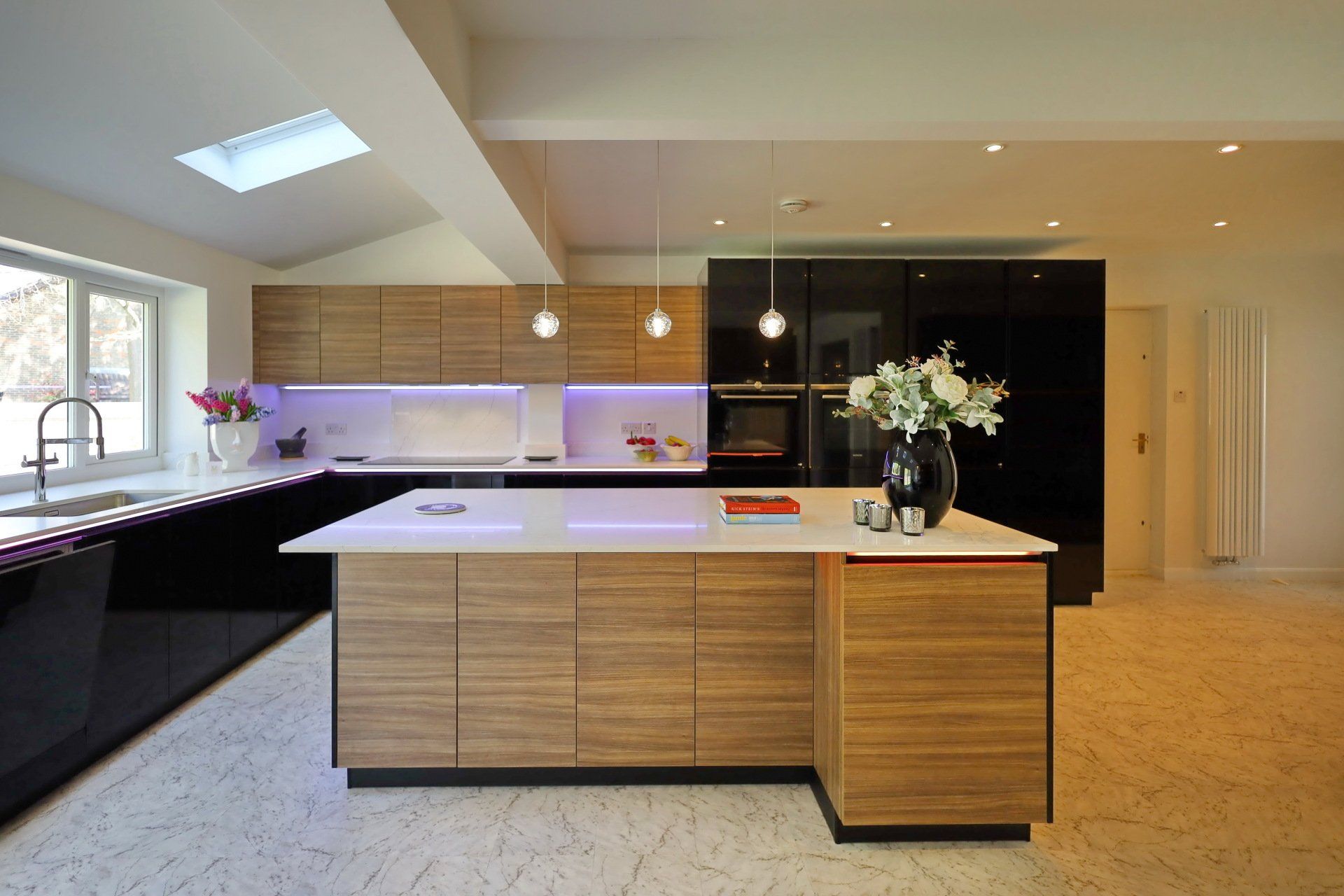 Modern kitchen with wooden and black cabinets, white countertops, and a central island with pendant lights.