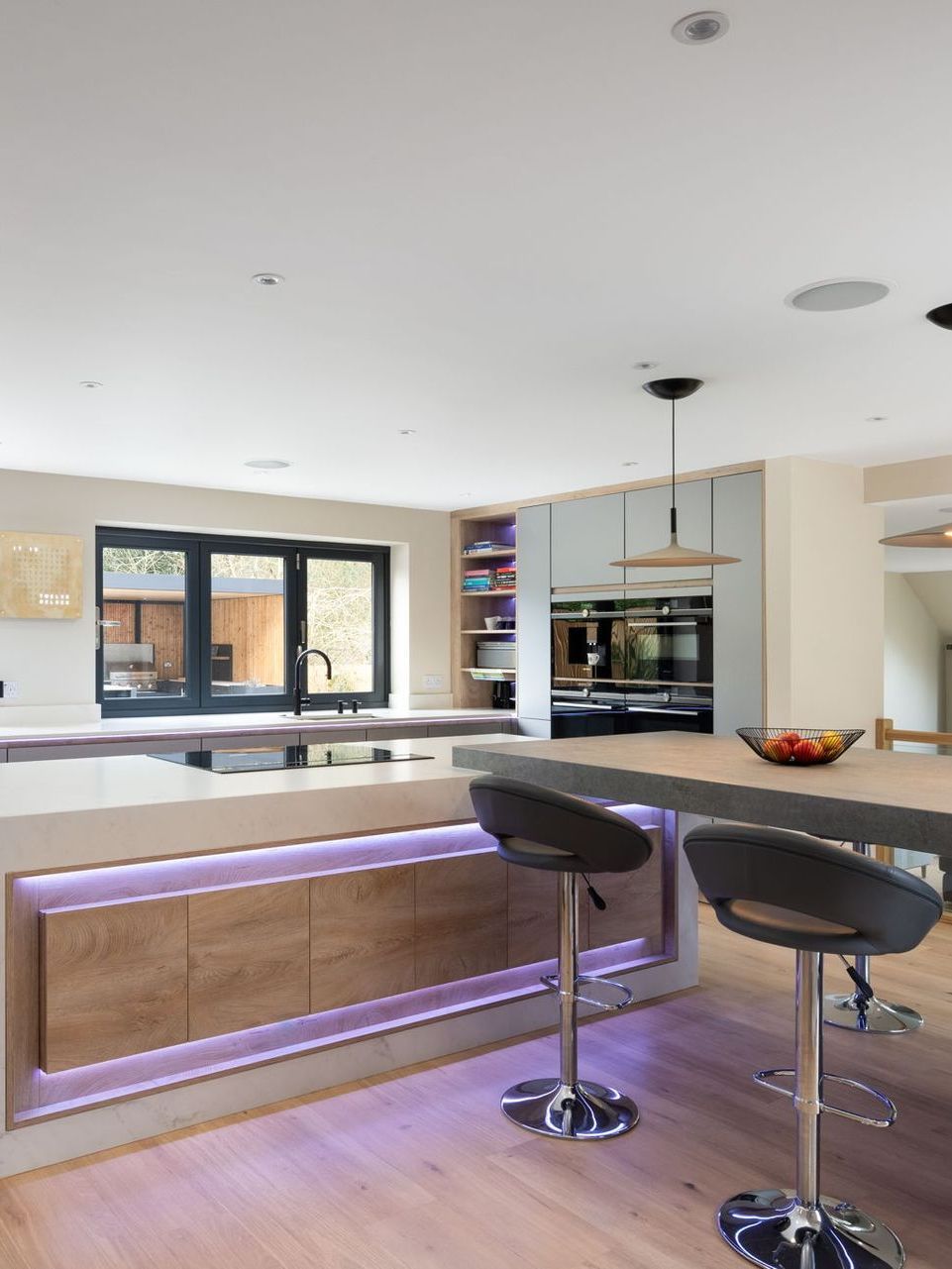 Modern kitchen with island, wooden cabinets, and bar stools. Purple LED lighting illuminates the base of the island.