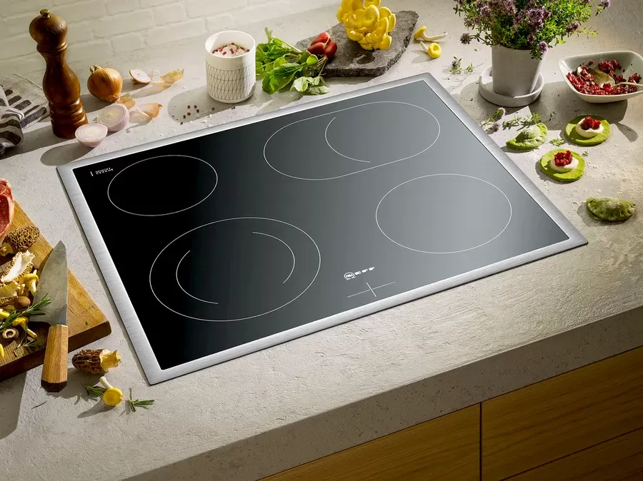 Black induction cooktop with four burners, surrounded by food items, on a countertop.