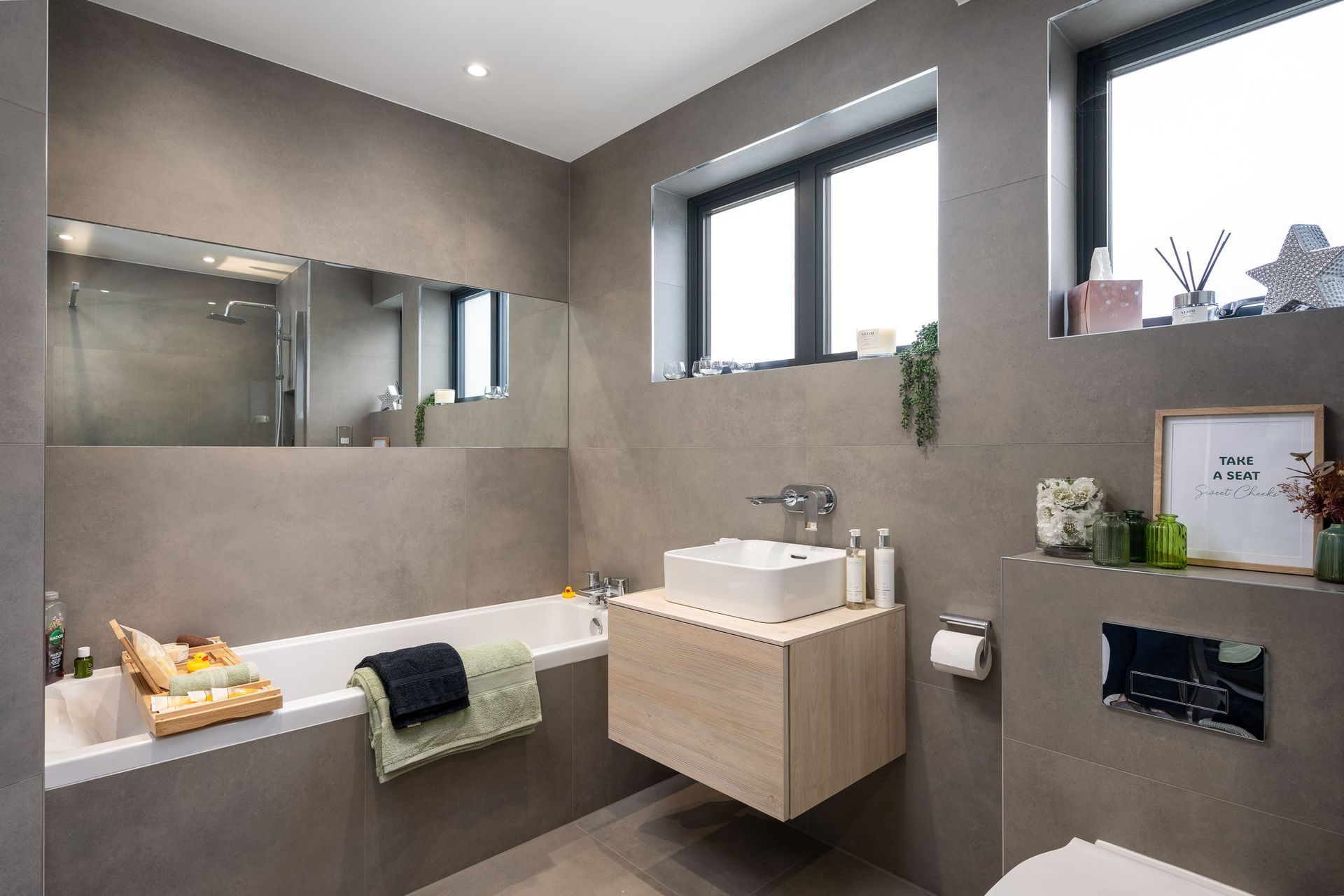 Modern bathroom with gray tiled walls, floating sink, bathtub, and window.