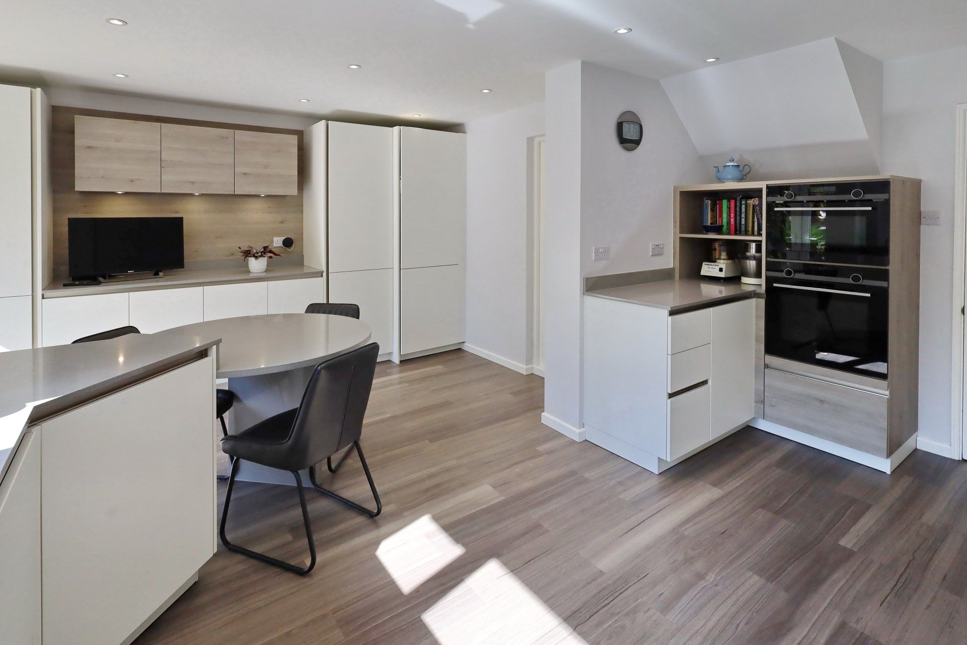 Modern kitchen with light wood floor, white and wood cabinets, and gray countertops.