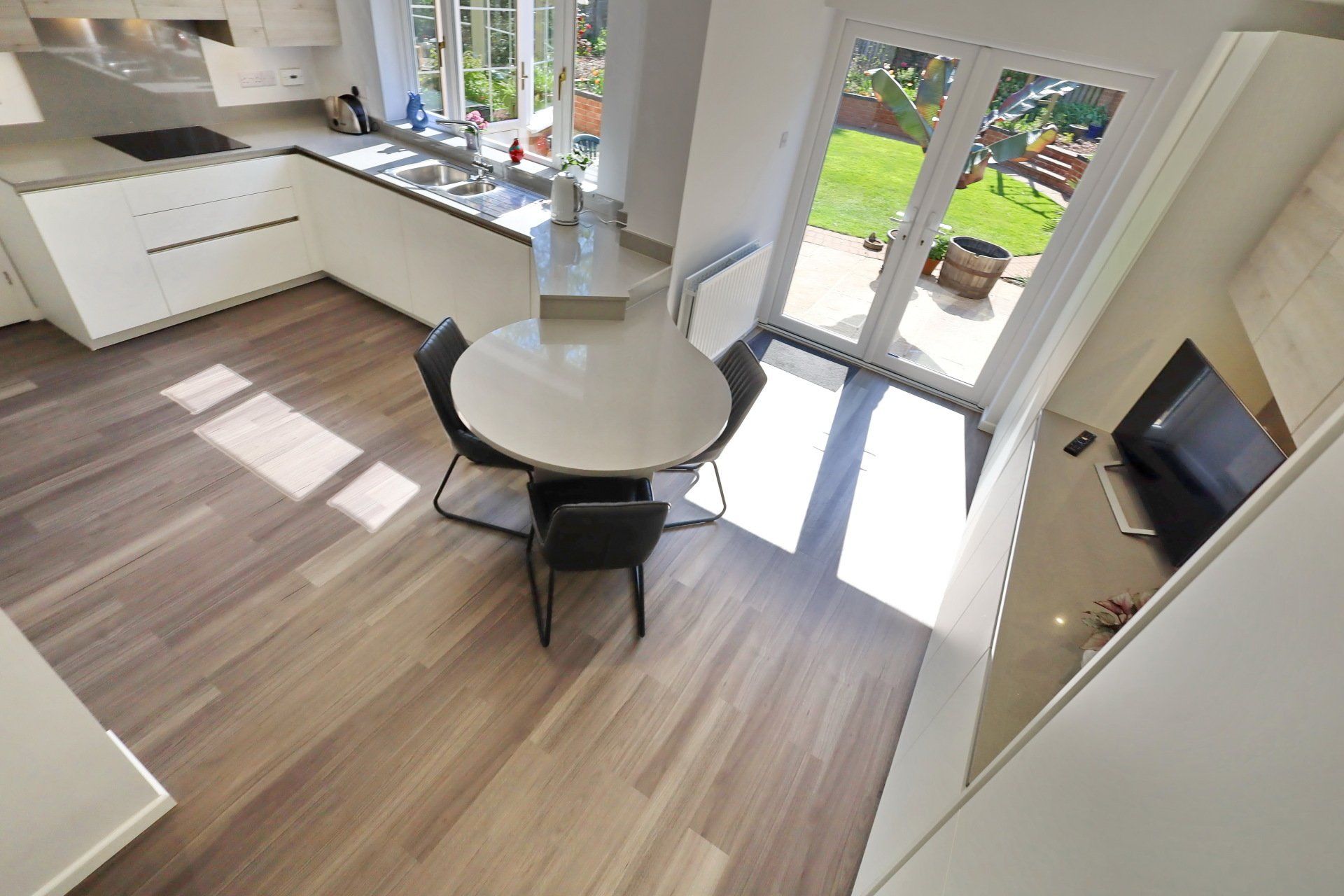 Modern kitchen with light wood floor, white cabinets, round table, chairs, and sliding glass door to a yard.
