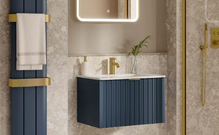 Blue vanity and gold fixtures in a modern bathroom, with a lit mirror and towel rack.