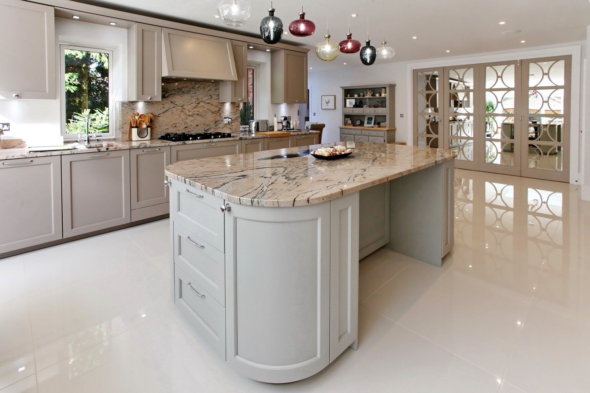 Elegant kitchen with light grey cabinetry, large island with granite countertop, and glass-paneled doors.