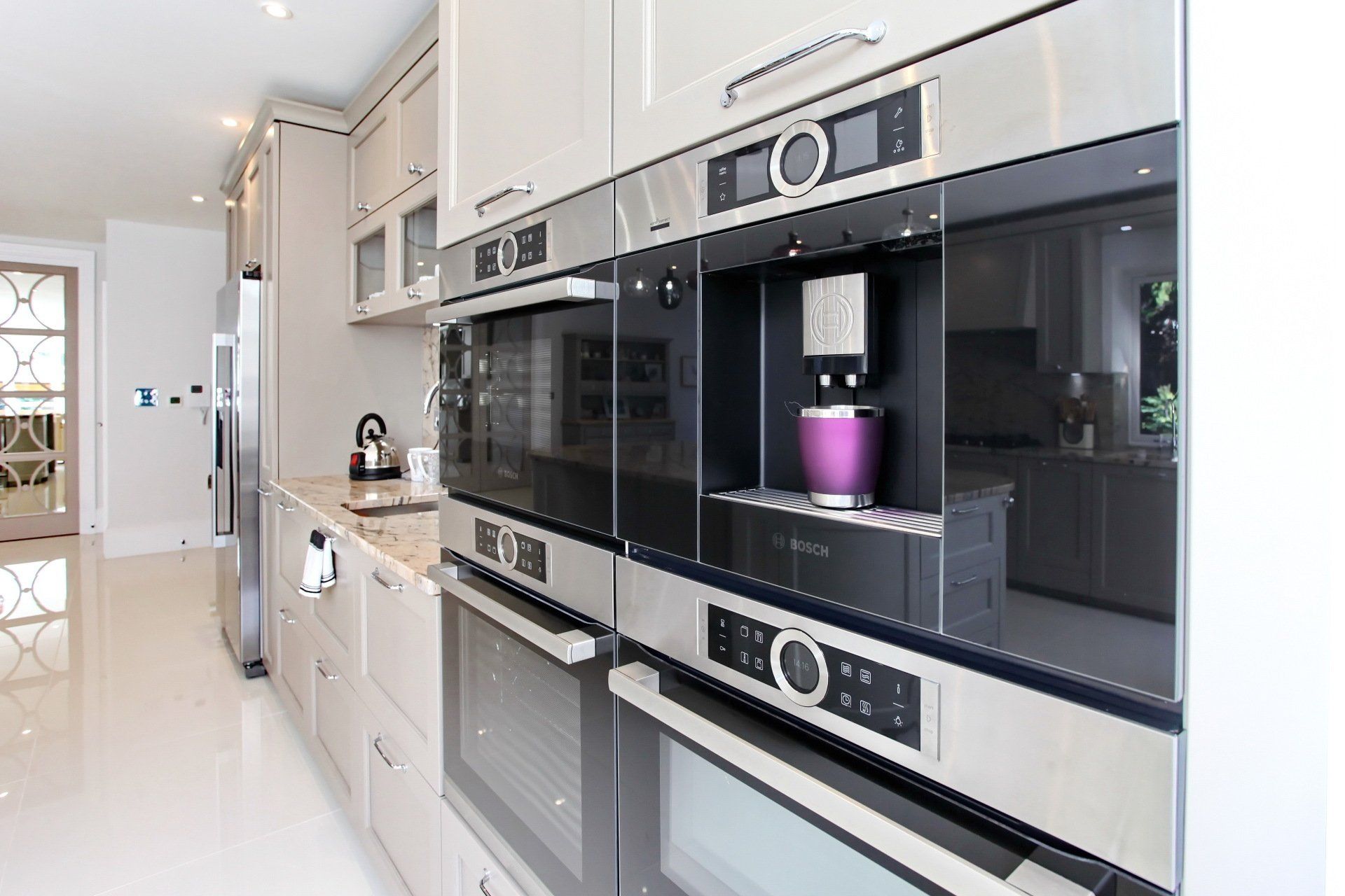 Modern kitchen with built-in appliances and light-colored cabinetry; stainless steel and black oven and coffee maker.