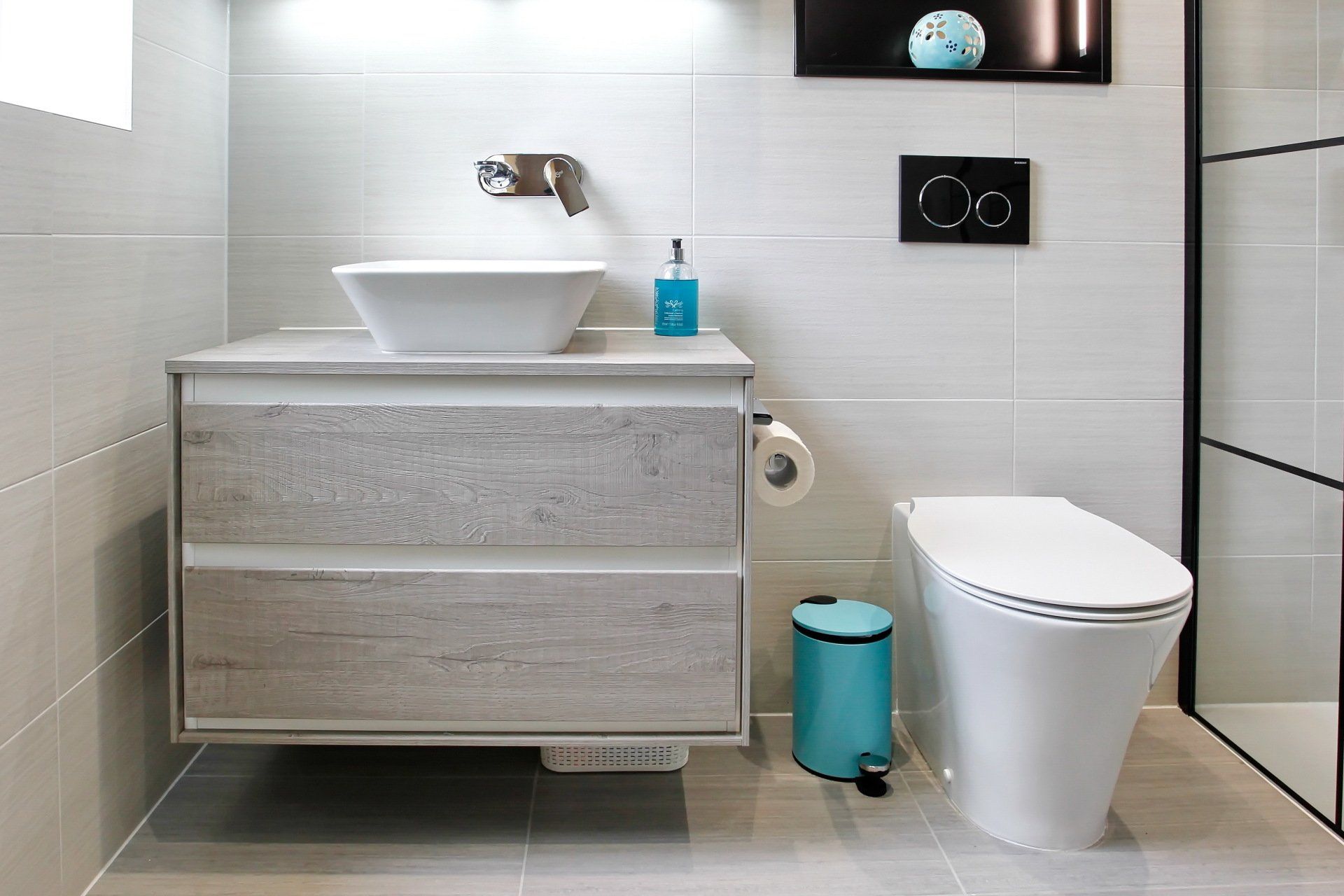 Modern bathroom with a floating vanity and toilet. Light gray tiles and accents. Turquoise trash can.