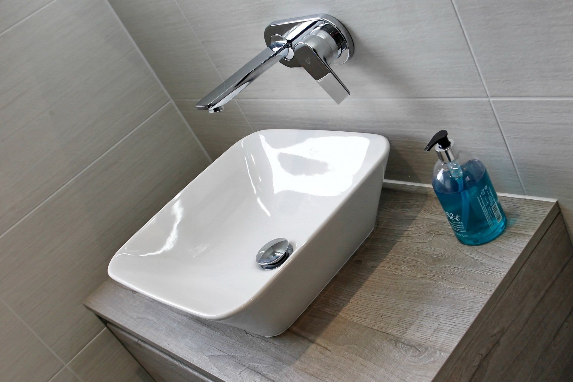 White ceramic sink with chrome faucet, on a gray countertop with soap.