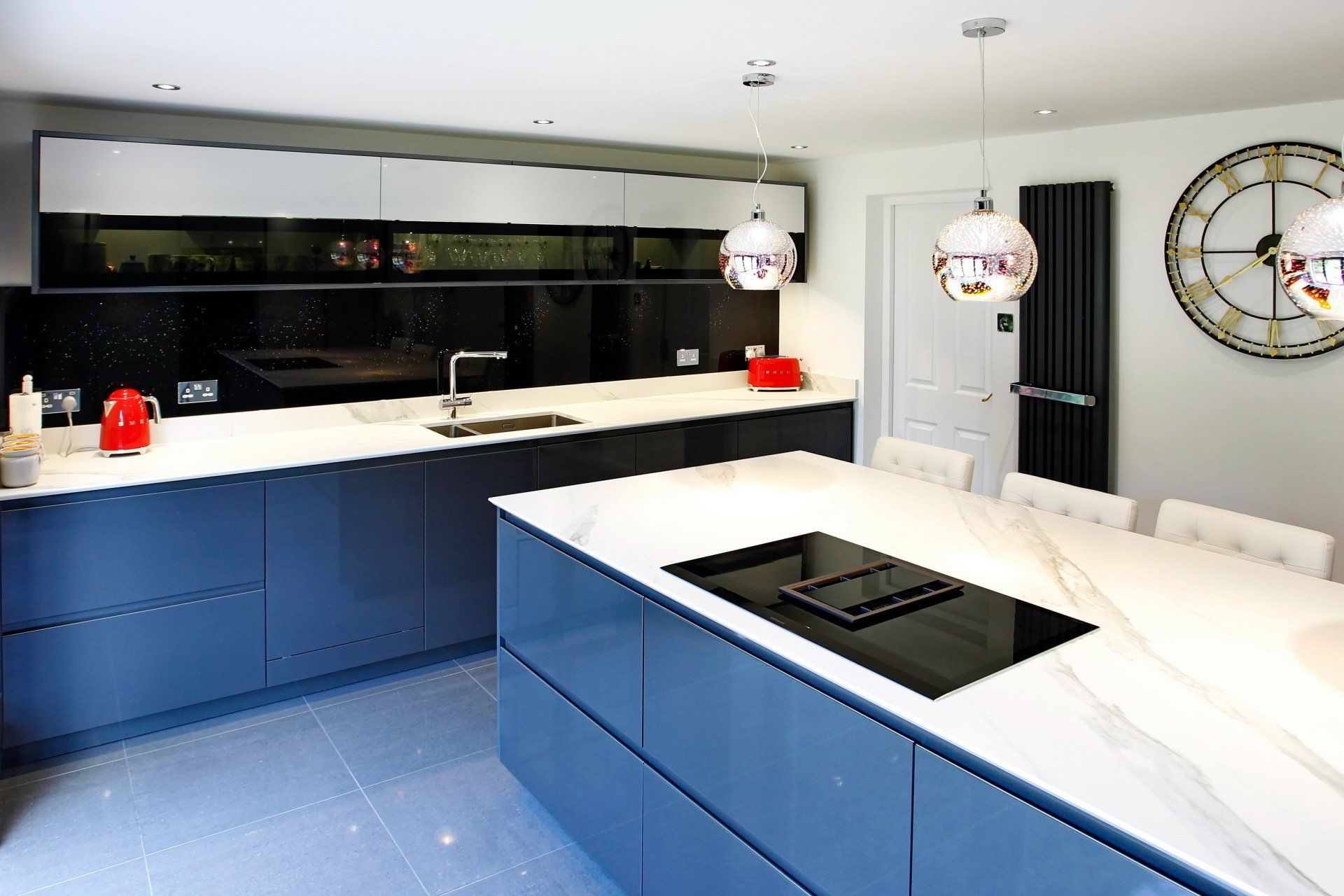 Modern kitchen with grey cabinets, white countertops, island with cooktop, and metallic pendant lights.