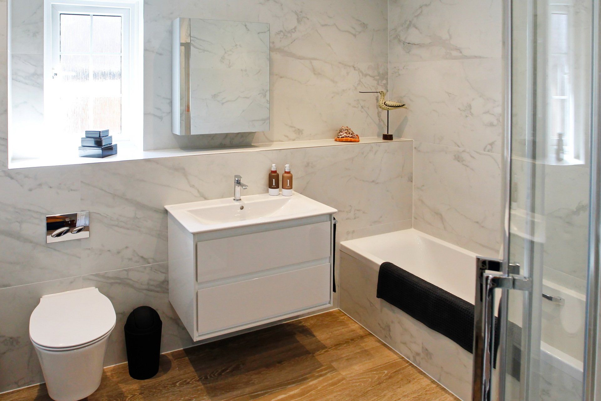 Modern bathroom with marble-look walls, floating vanity, toilet, bathtub, and shower enclosure.