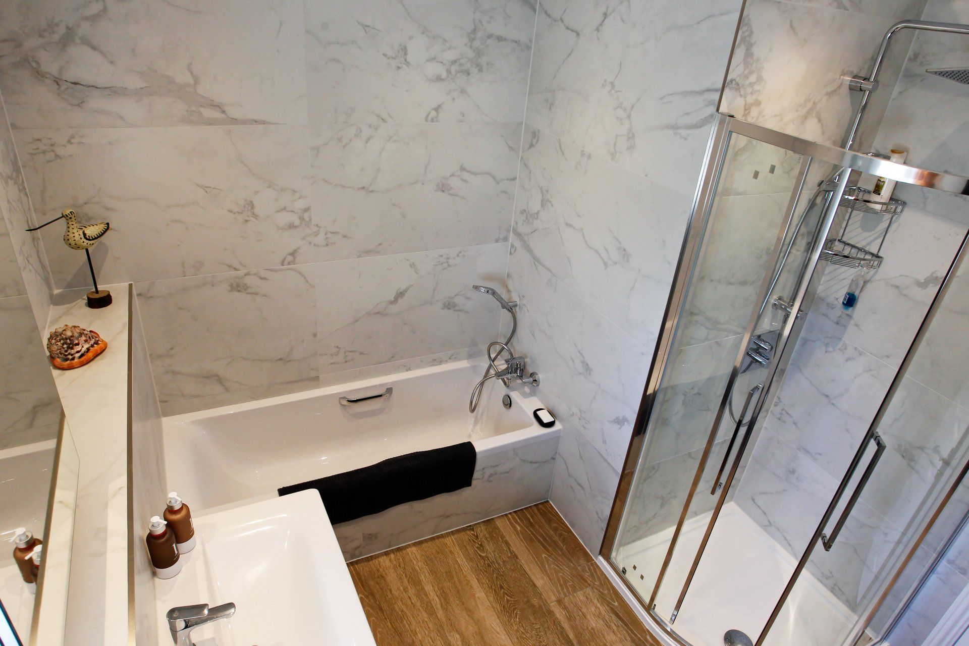 Bathroom with a bathtub, shower, sink, and marble-like tile. The floor is wood-like.