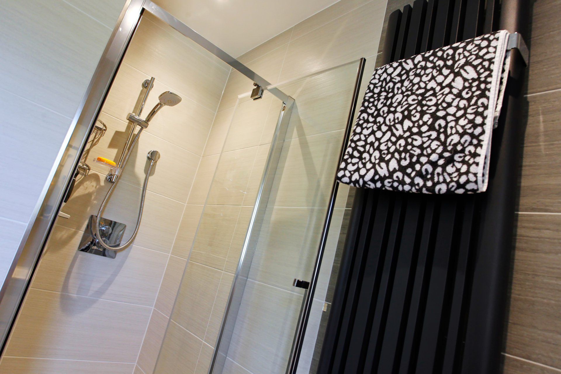 Shower stall next to black towel radiator with a patterned towel in a bathroom.
