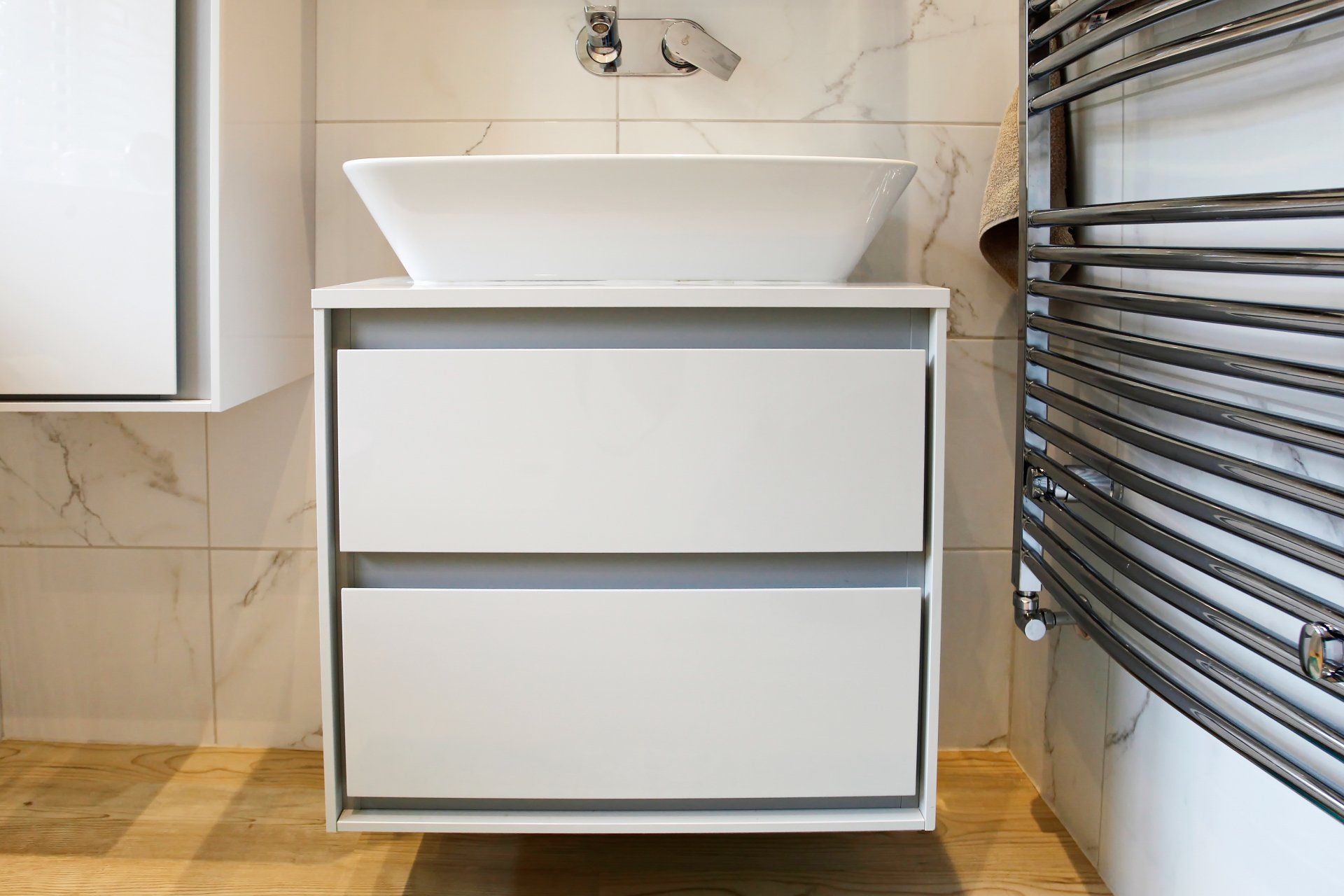 White floating bathroom vanity with a vessel sink and two drawers. A towel rack is on the right.