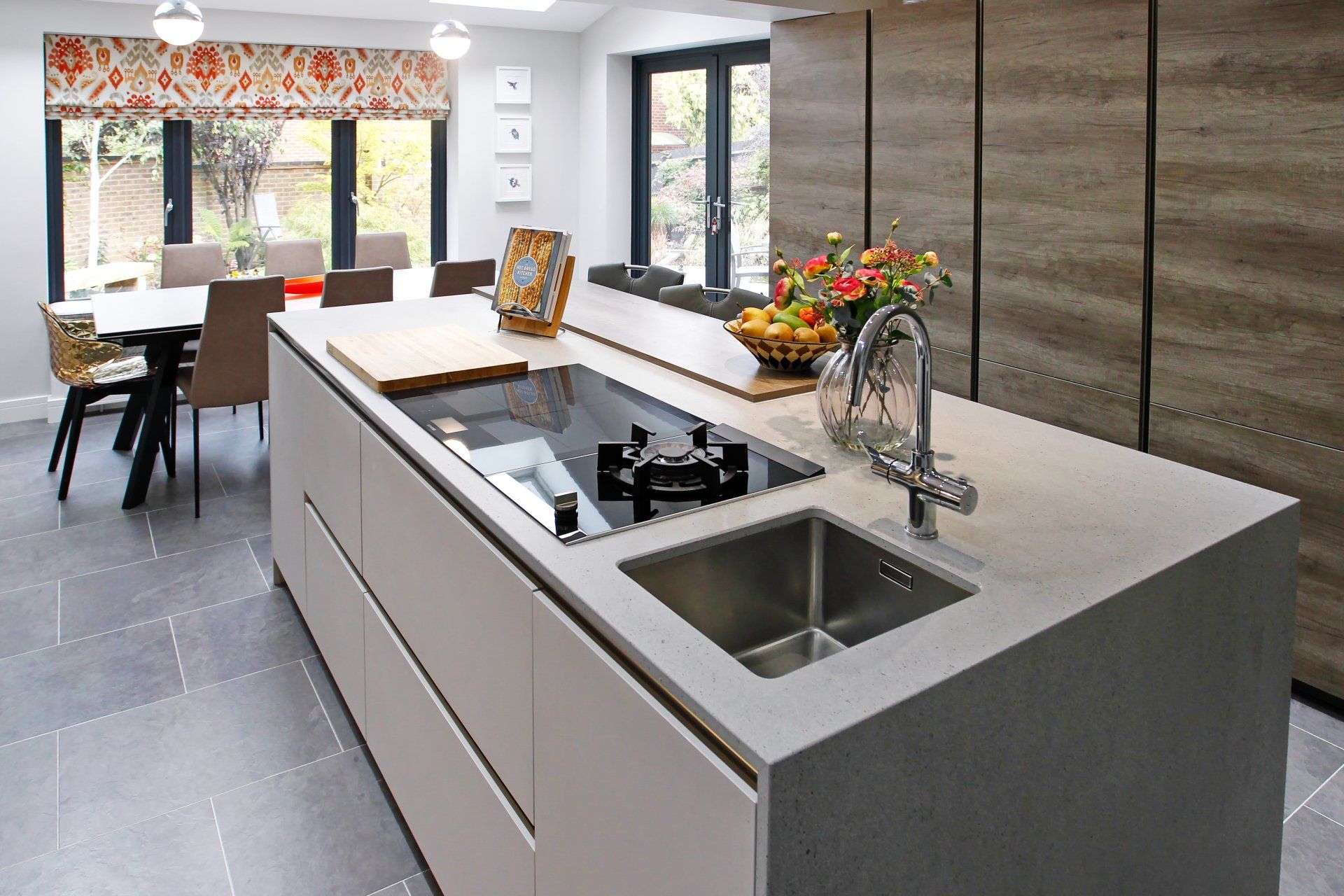 Modern kitchen with island, cooktop, sink, and dining area with large windows, neutral tones.
