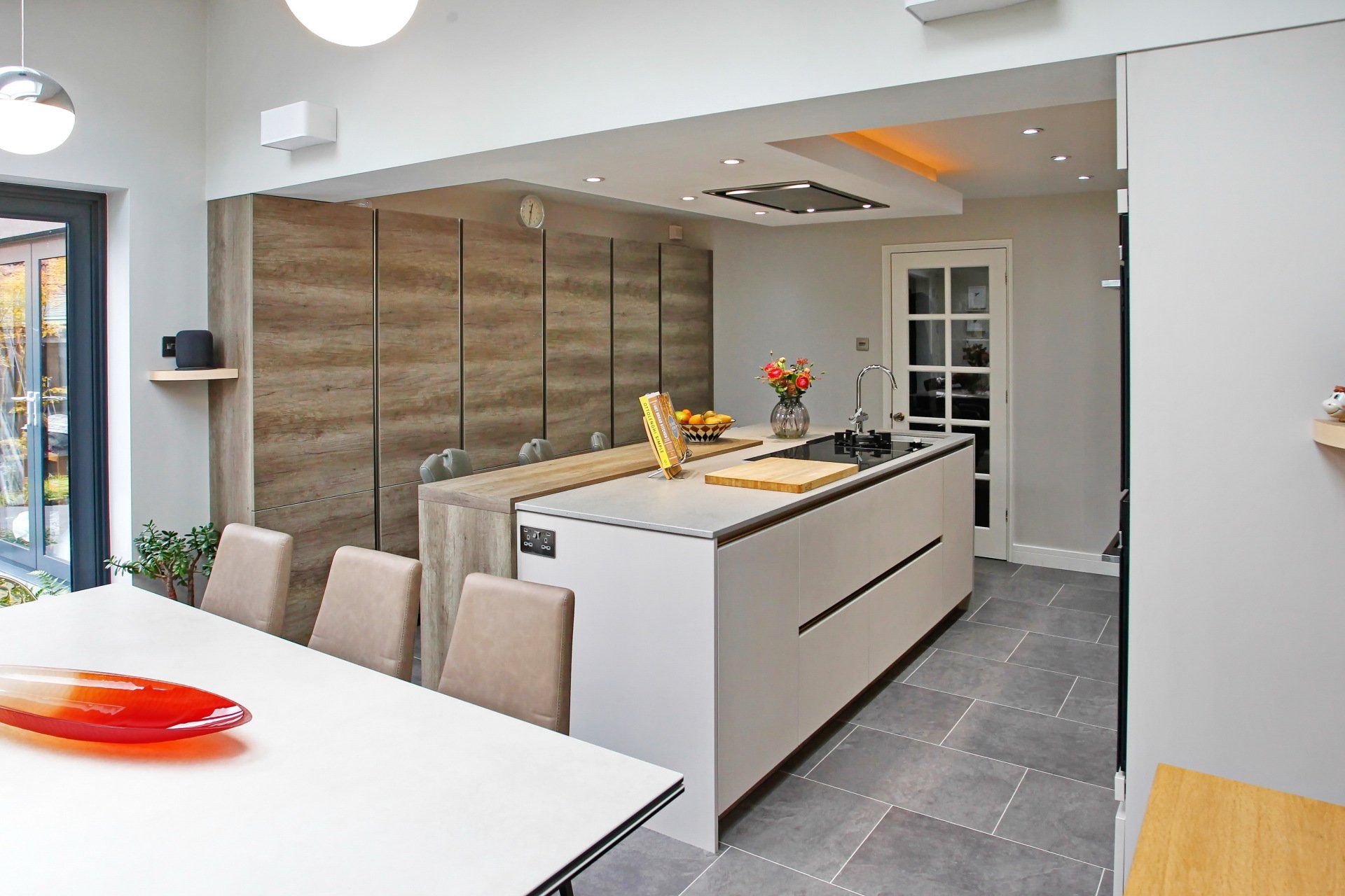 Modern kitchen with white island, wood cabinets, dining table, and gray tile floor.