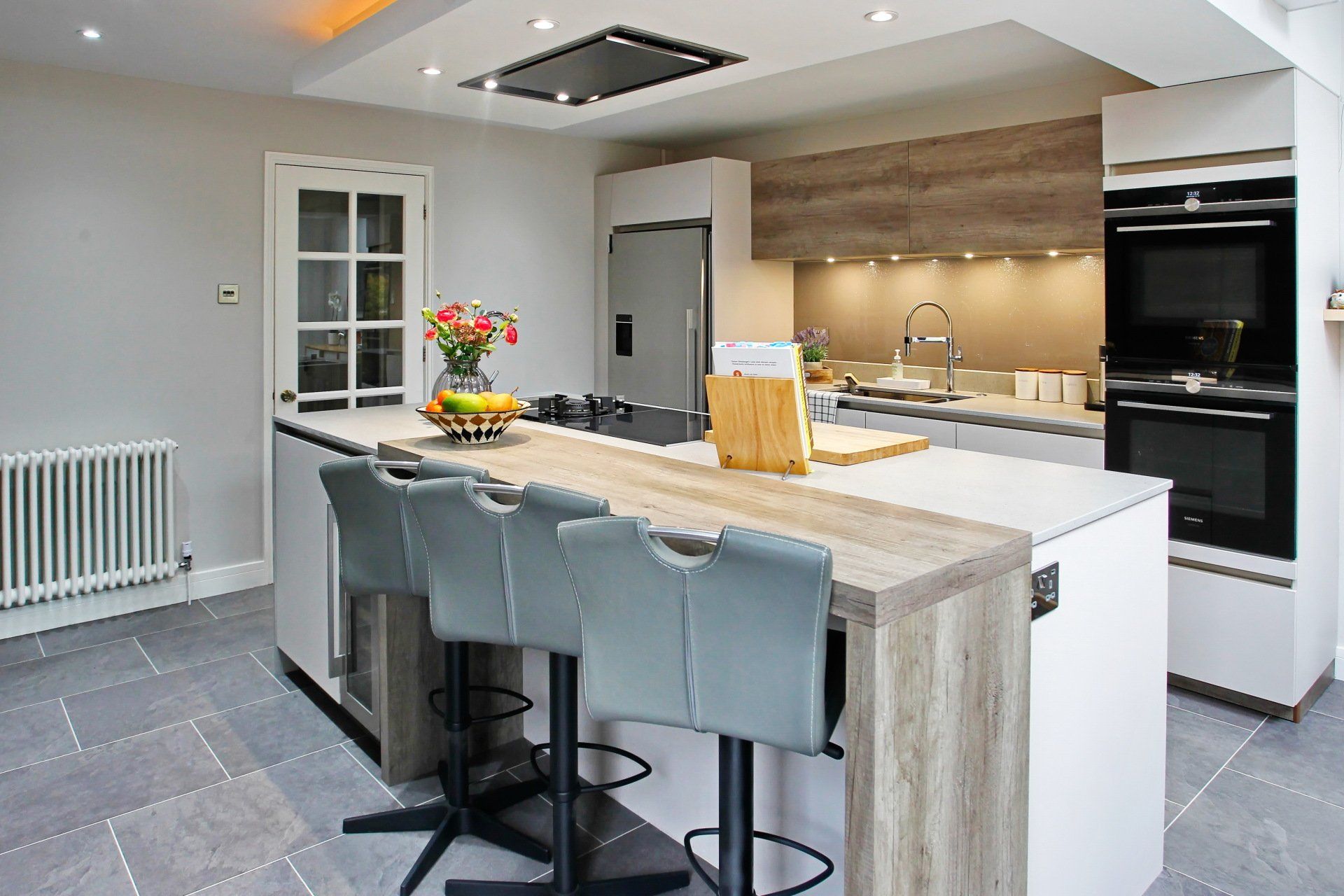 Modern kitchen with island, seating, wood accents, and stainless steel appliances.