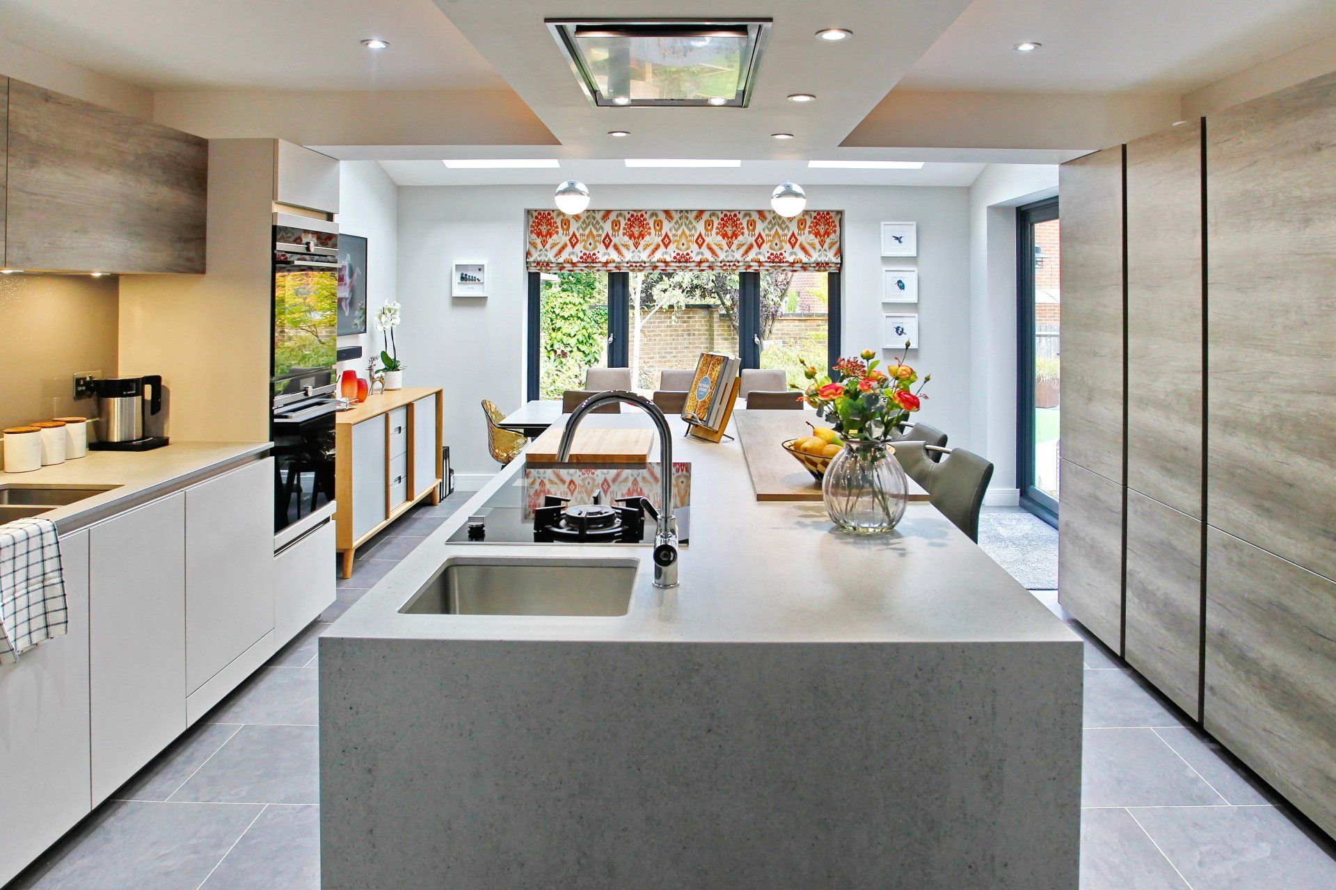 Modern kitchen with white countertops, grey island, and a dining area with floral window treatment.