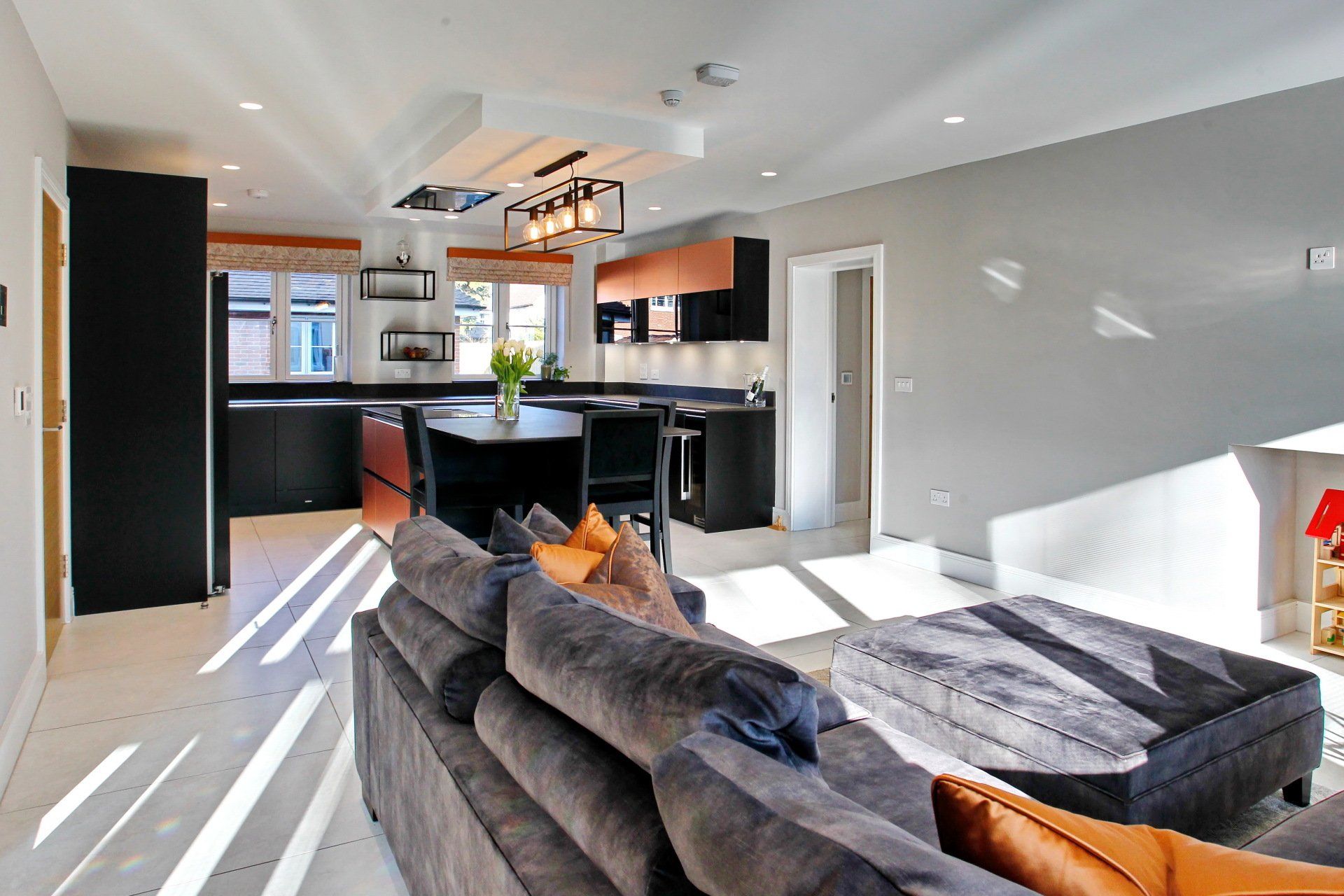 Open-plan kitchen and living room with black cabinetry, copper accents, gray sofa, and natural light.