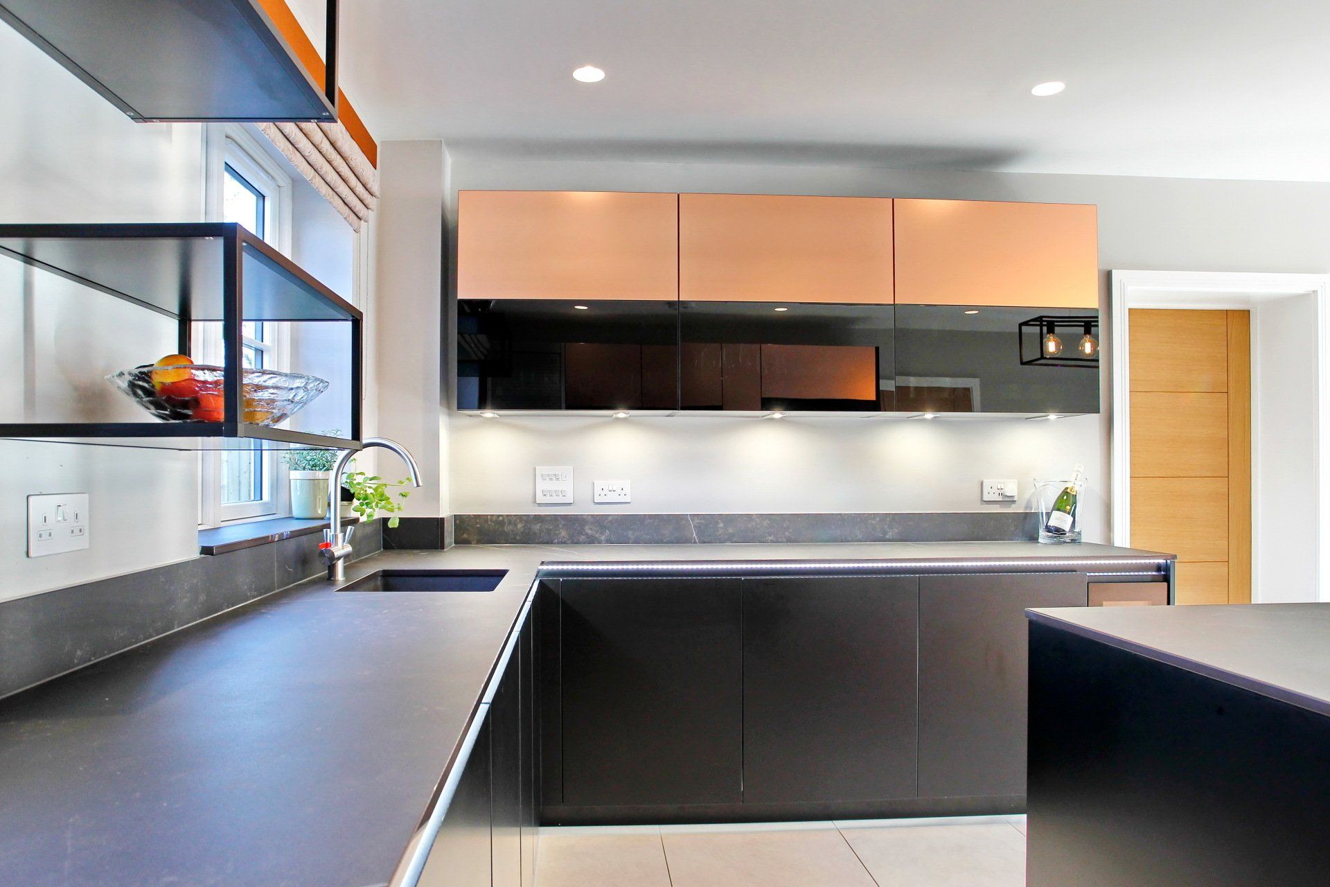 Modern kitchen with dark countertops, cabinets, and light-colored upper cabinets.