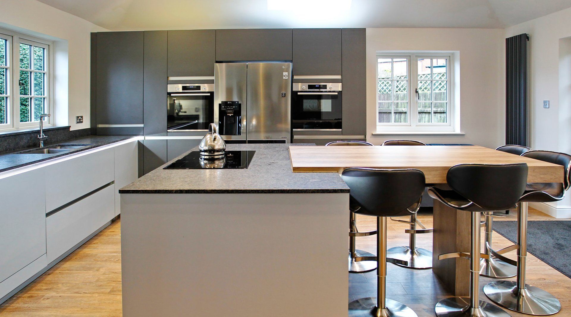 Modern kitchen with gray and white cabinets, stainless steel appliances, and a wooden island with bar stools.