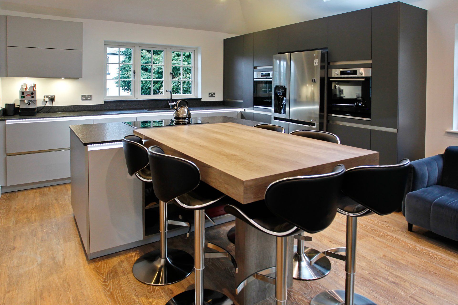 Modern kitchen with an island, dark gray cabinets, stainless steel appliances, and wood floors.
