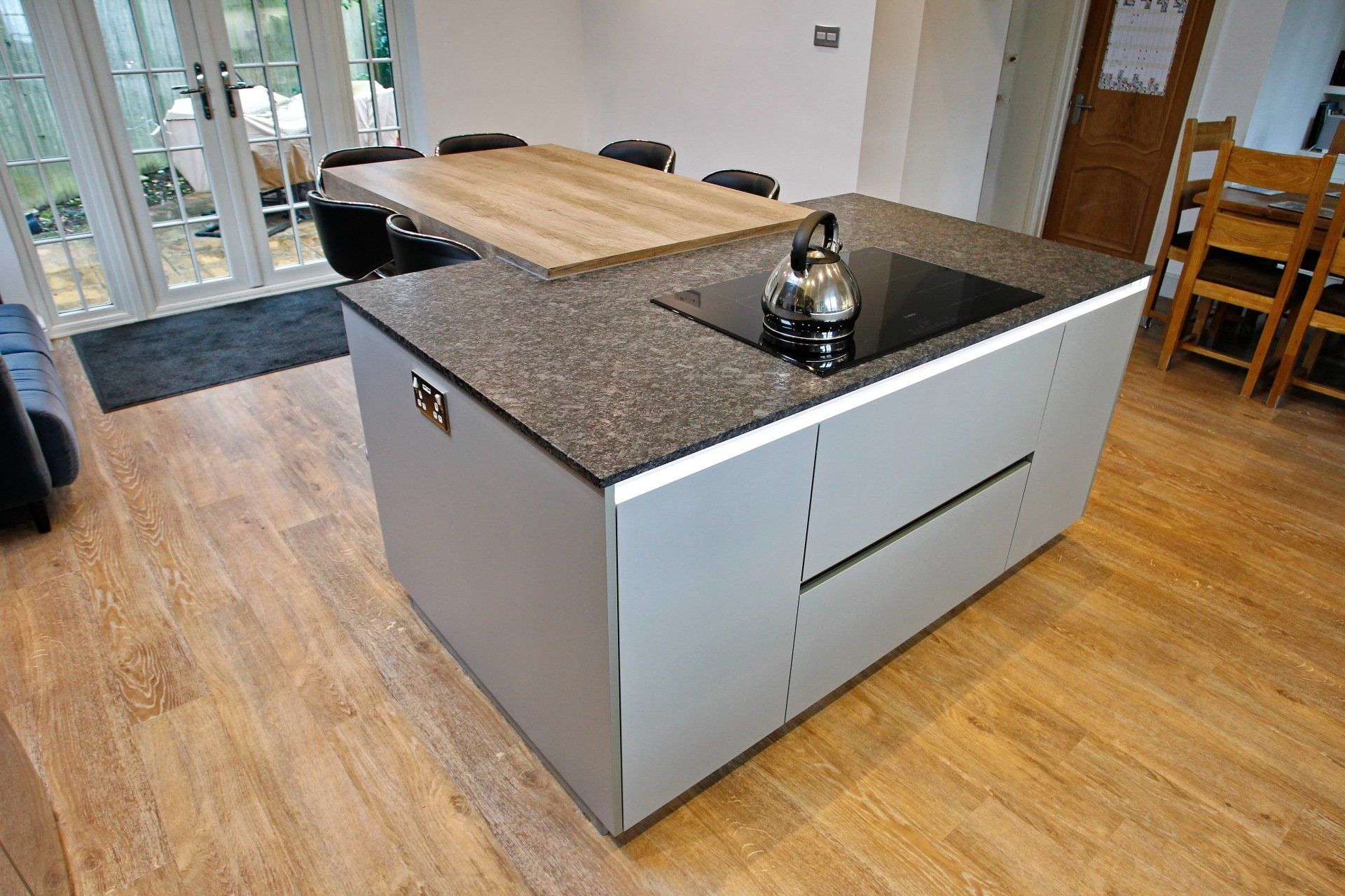 Modern kitchen island with granite countertop, stovetop, and attached wooden dining table.